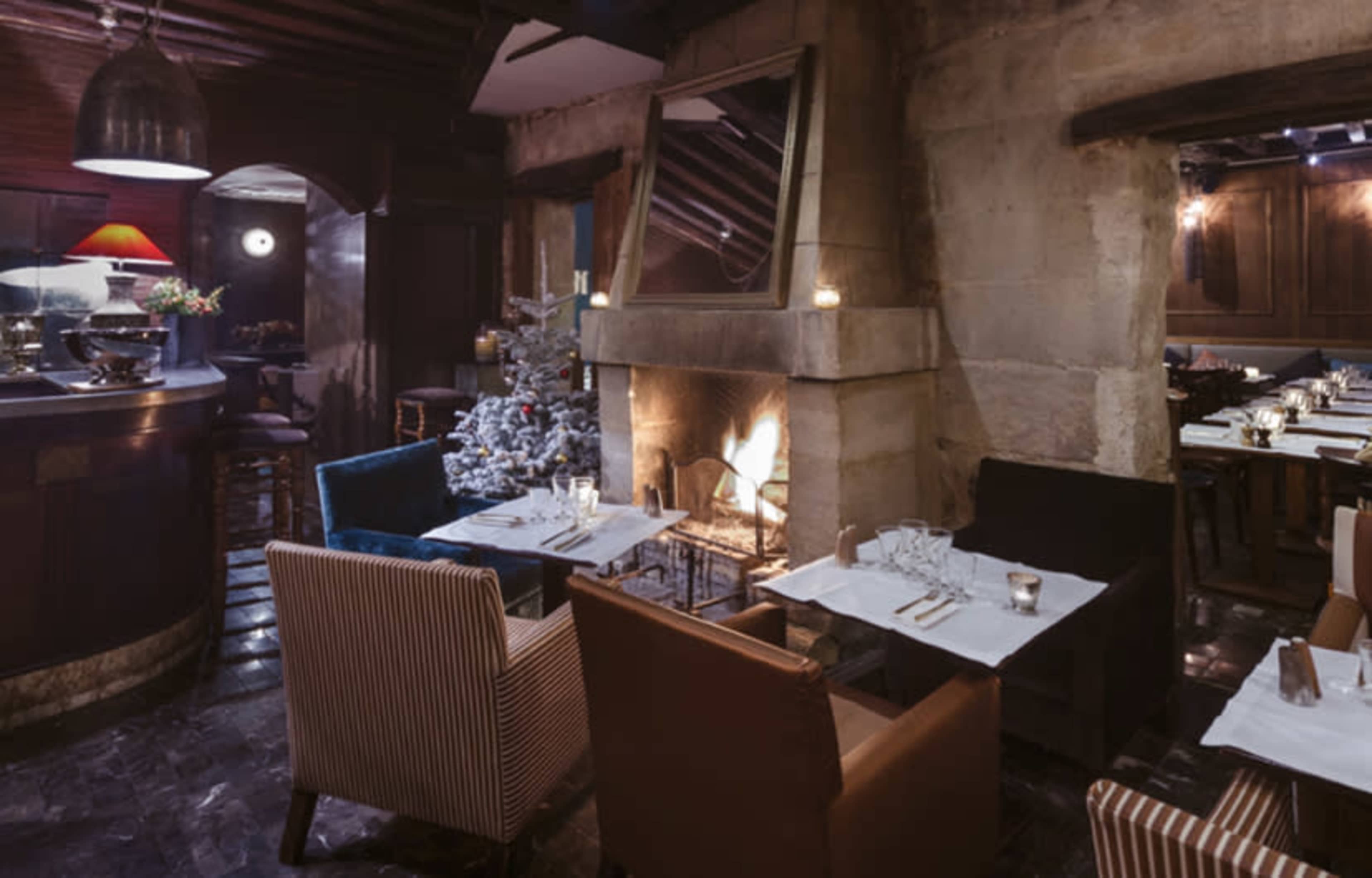 A cozy restaurant interior featuring a fireplace, wooden beams, and tables set for dining.