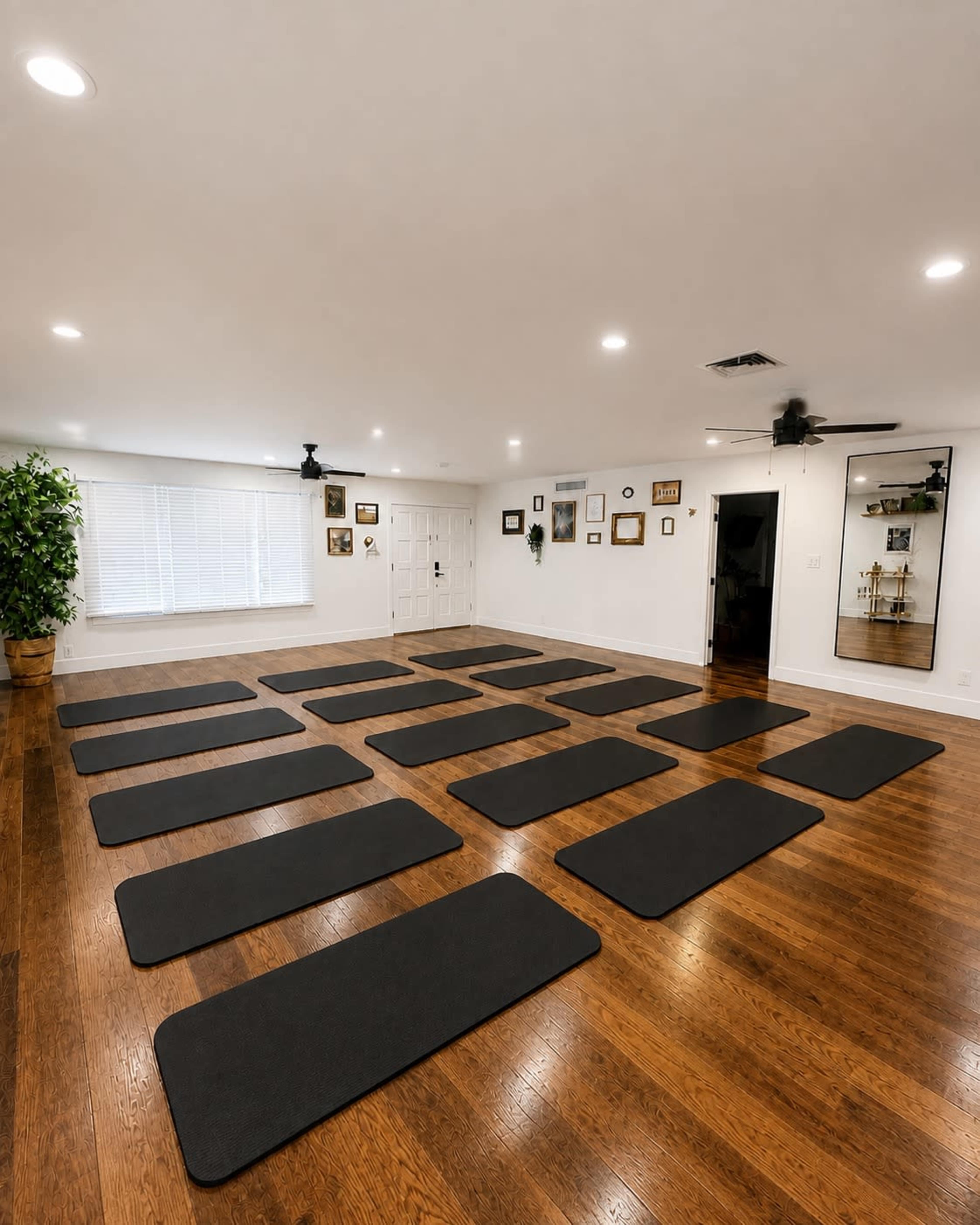The image shows a yoga or exercise studio with several black mats arranged evenly on a wooden floor.