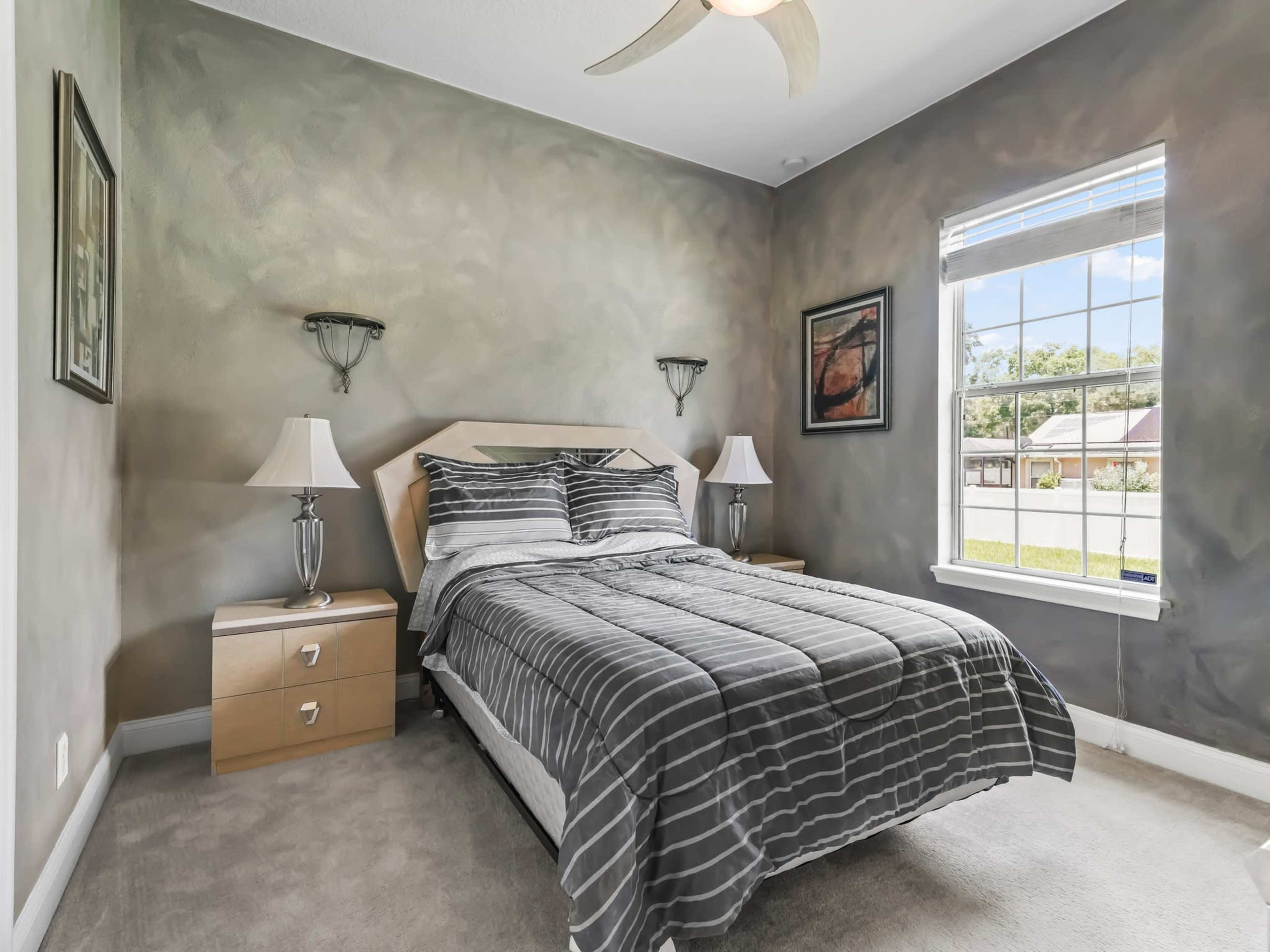 A neatly arranged bedroom features a striped bedspread, two bedside lamps, and windows allowing natural light.