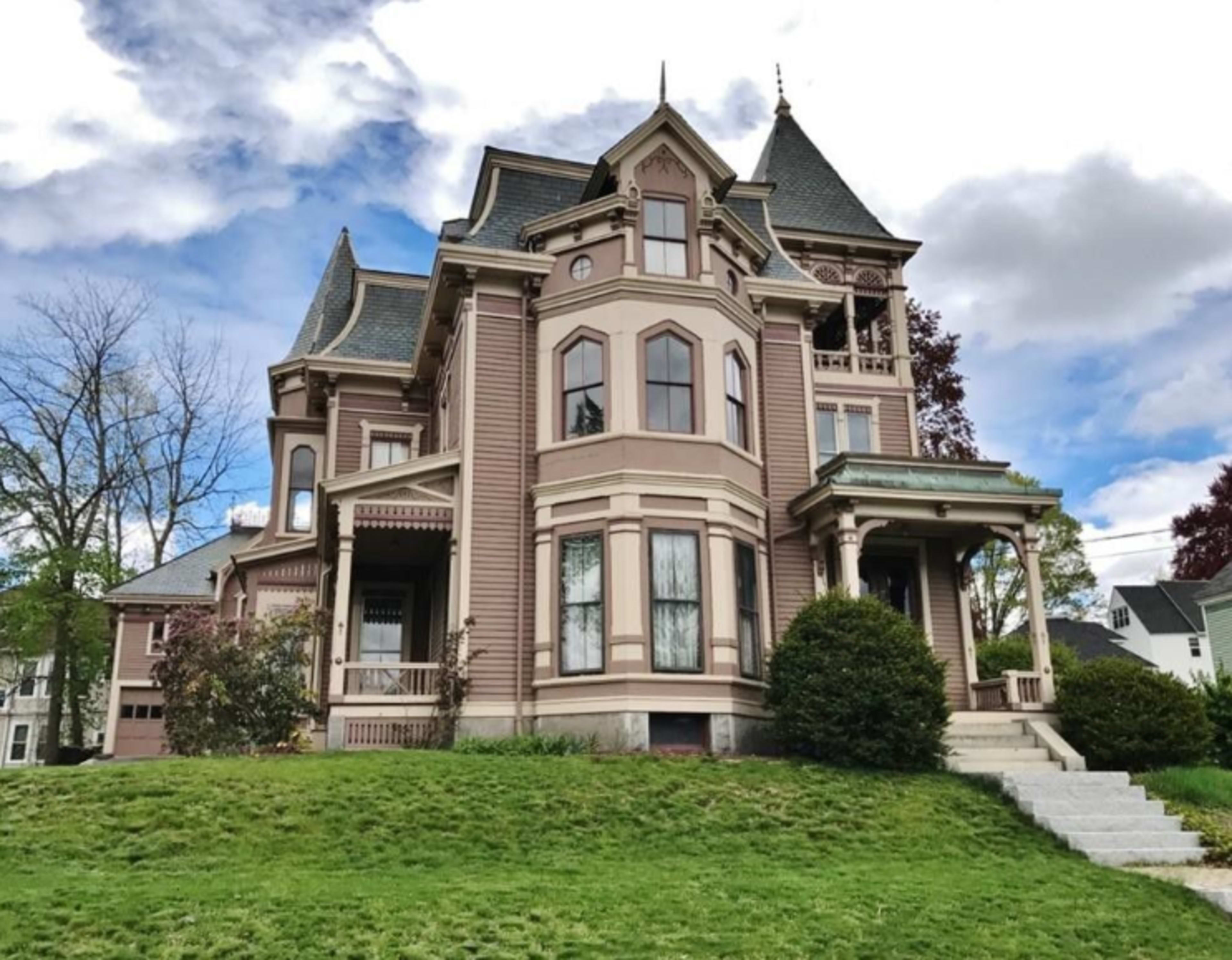 A large Victorian-style house with a steep roof and ornate details is situated on a green lawn.