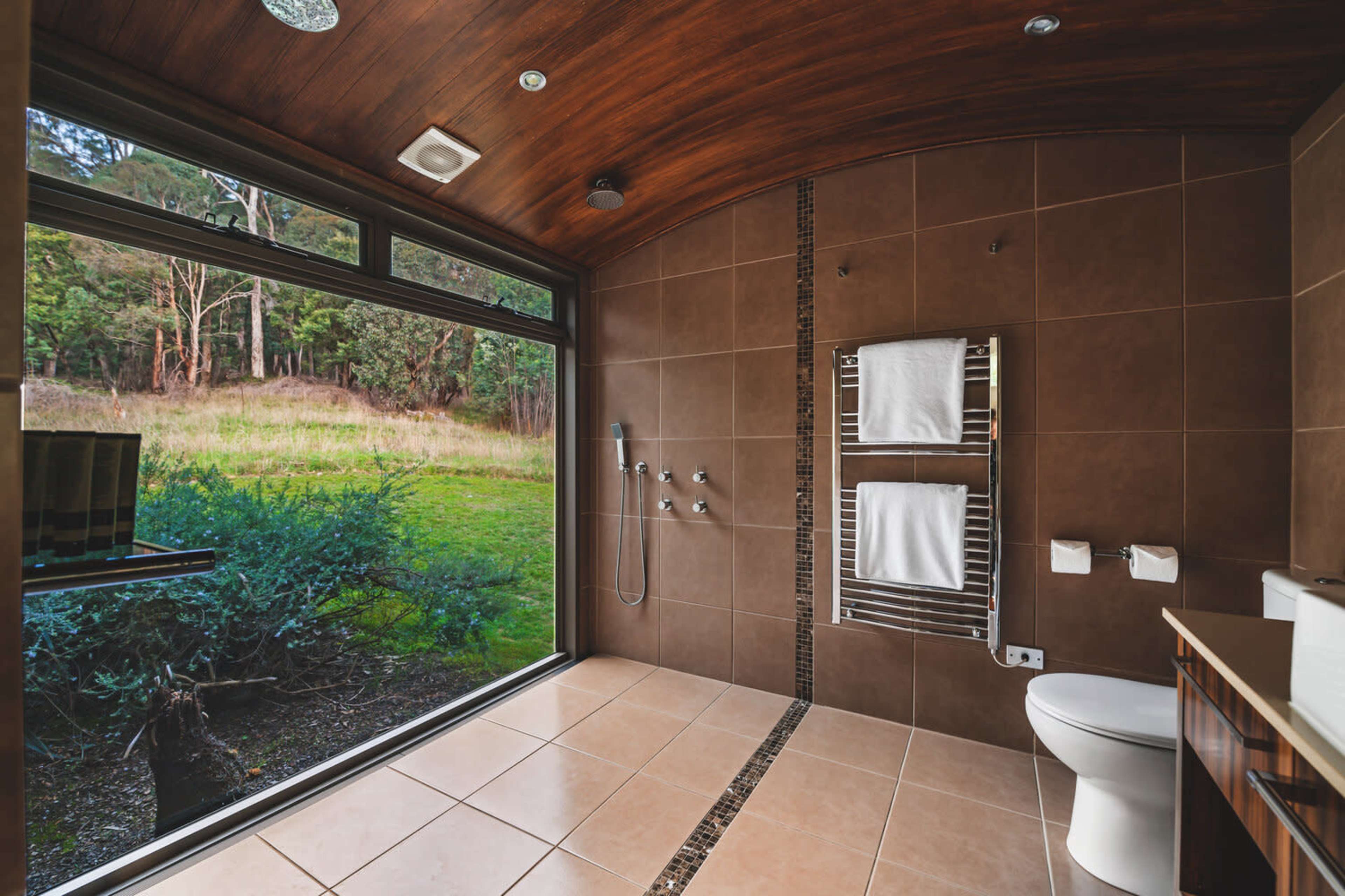 The bathroom features a large window overlooking a green landscape, tiled flooring, a toilet, and dual towel racks.