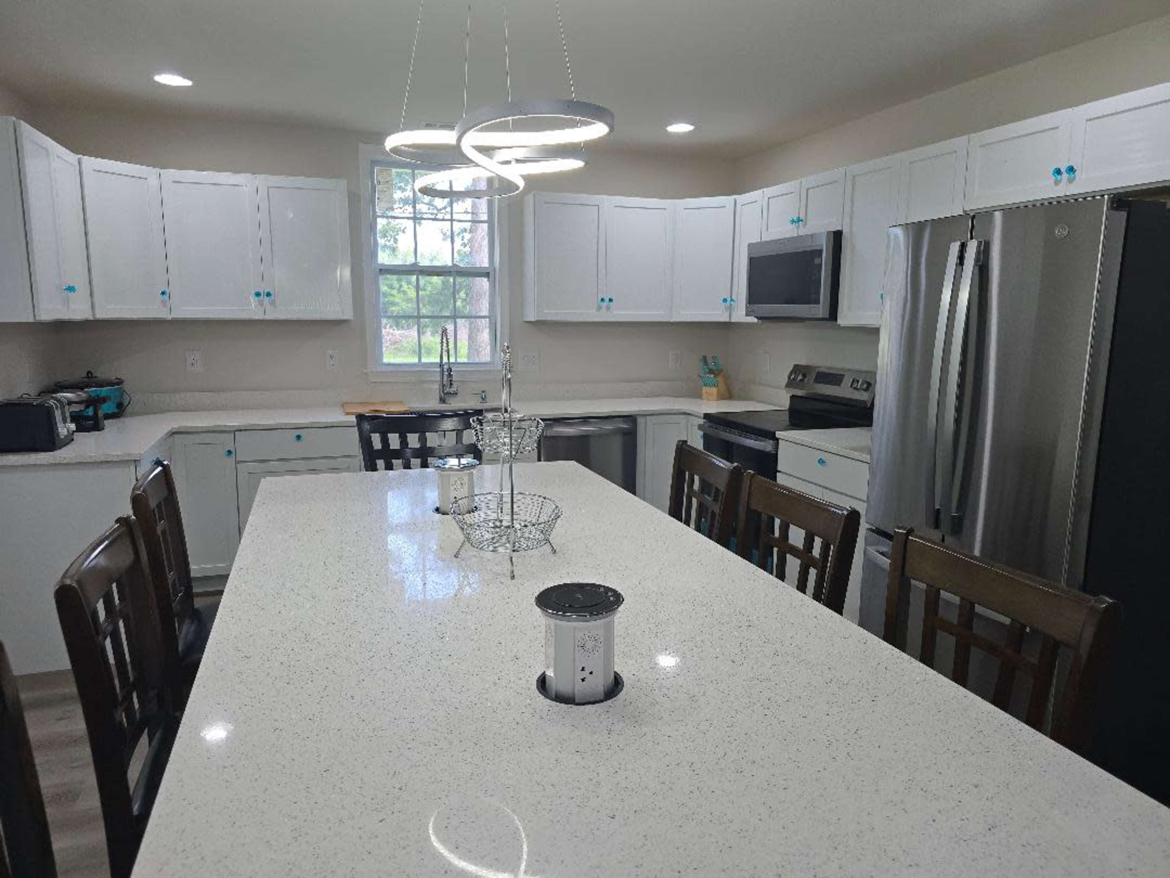 The image shows a modern kitchen with white cabinets, a large island with a quartz countertop, and stainless steel appliances.
