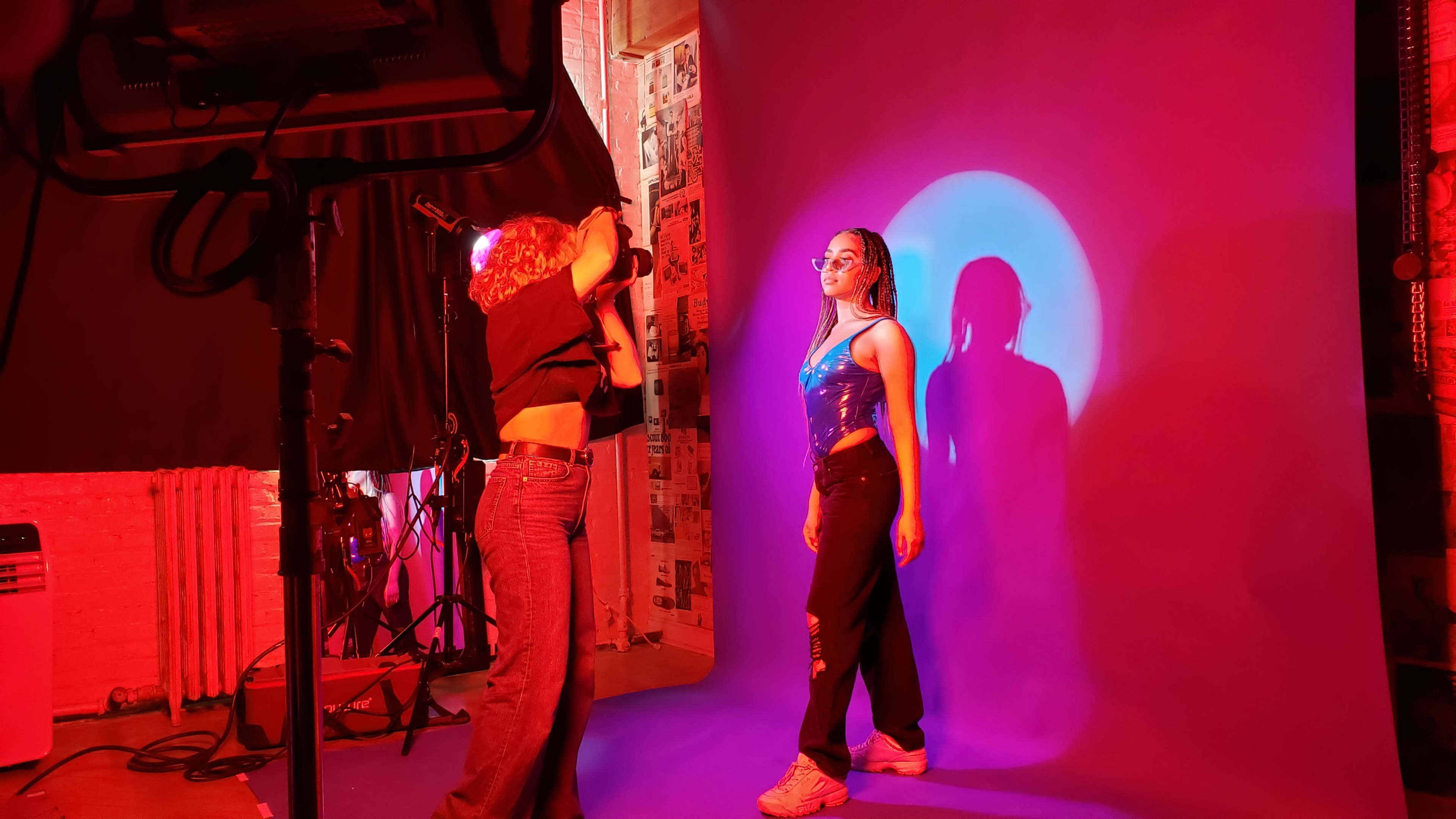 A photographer captures a model posing against a brightly lit purple backdrop in a studio setting.