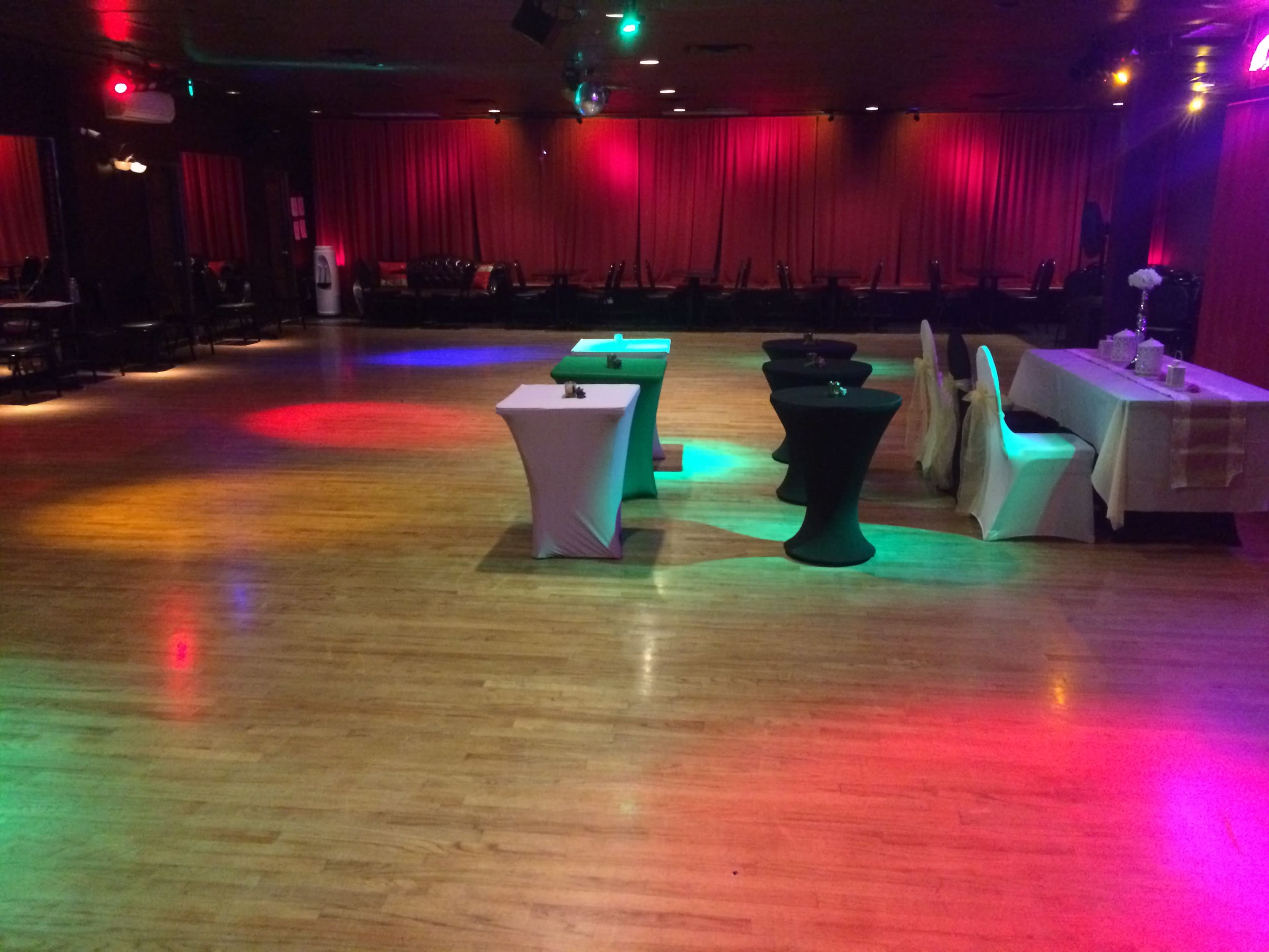 An empty event space with several tables draped in various colors and illuminated by multicolored lights.