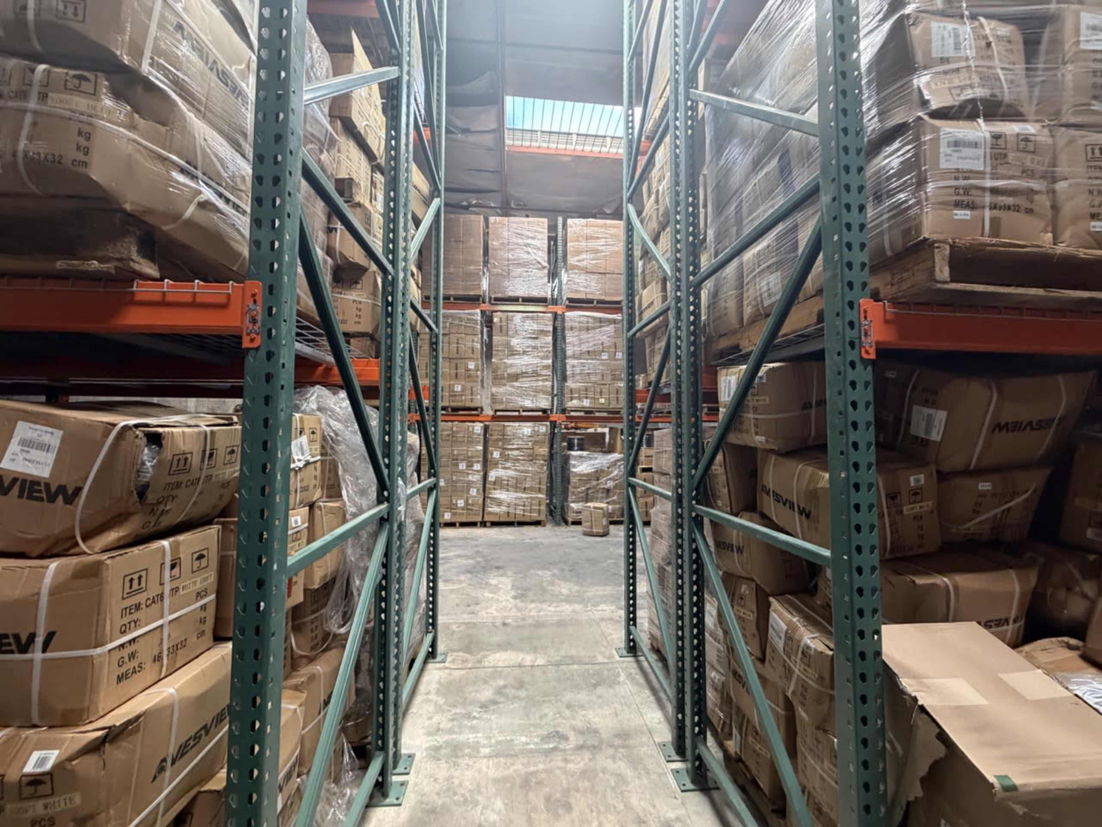 A narrow aisle in a warehouse is lined with tall shelves stacked with neatly packed boxes.
