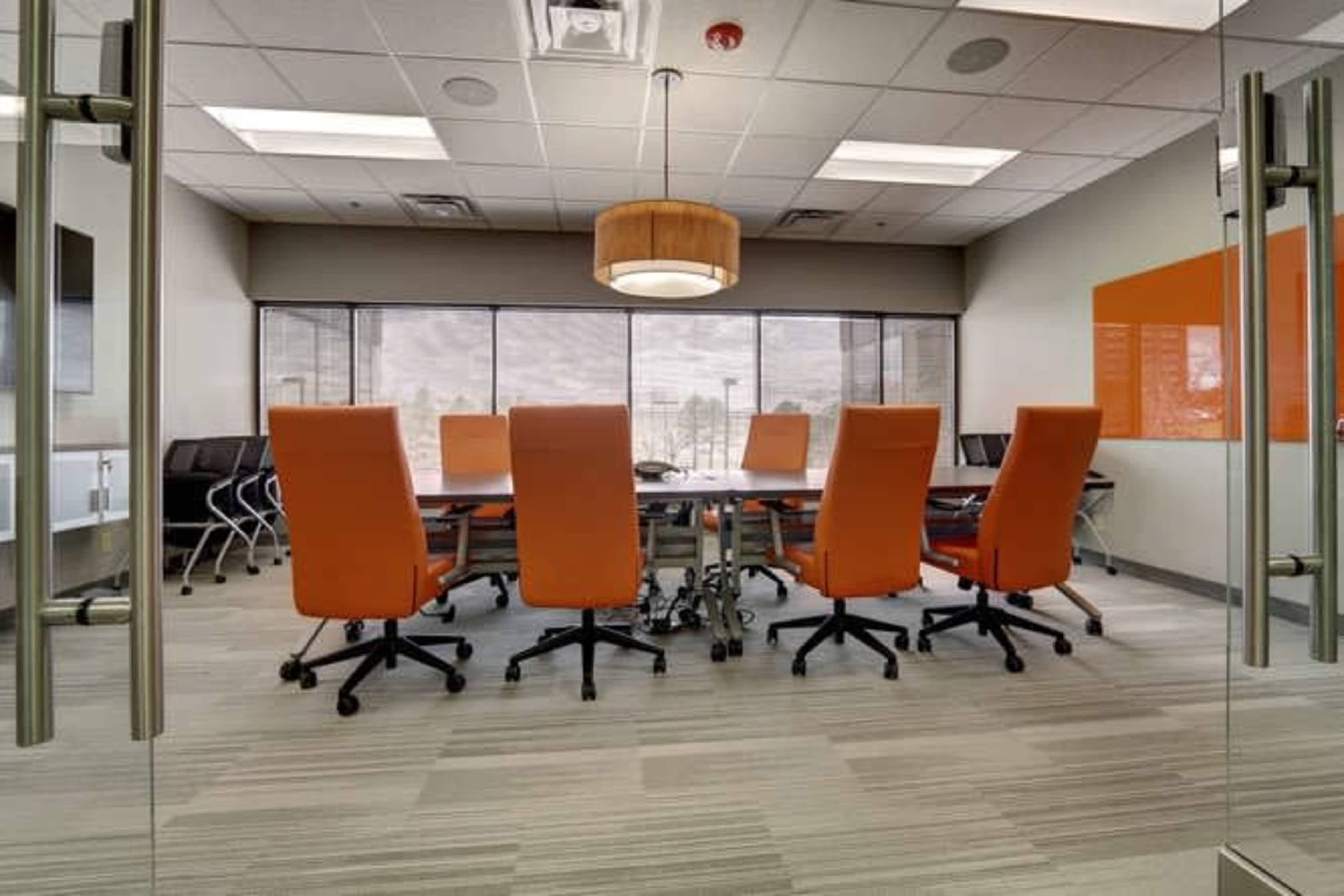 A modern conference room features a large table surrounded by orange chairs and large windows overlooking a cityscape.