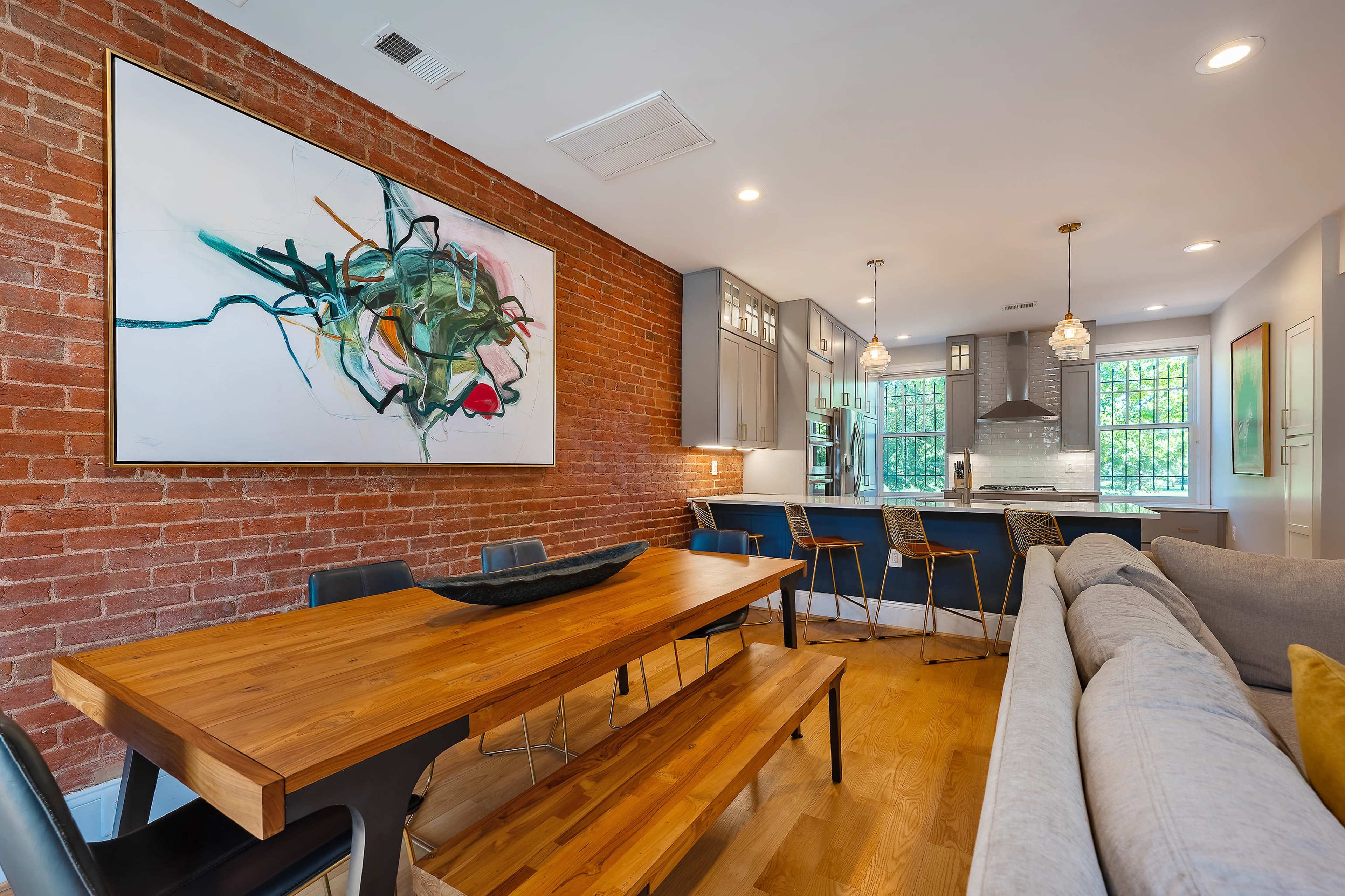 A modern living and dining area with a wooden dining table, brick walls, and a kitchen visible in the background.