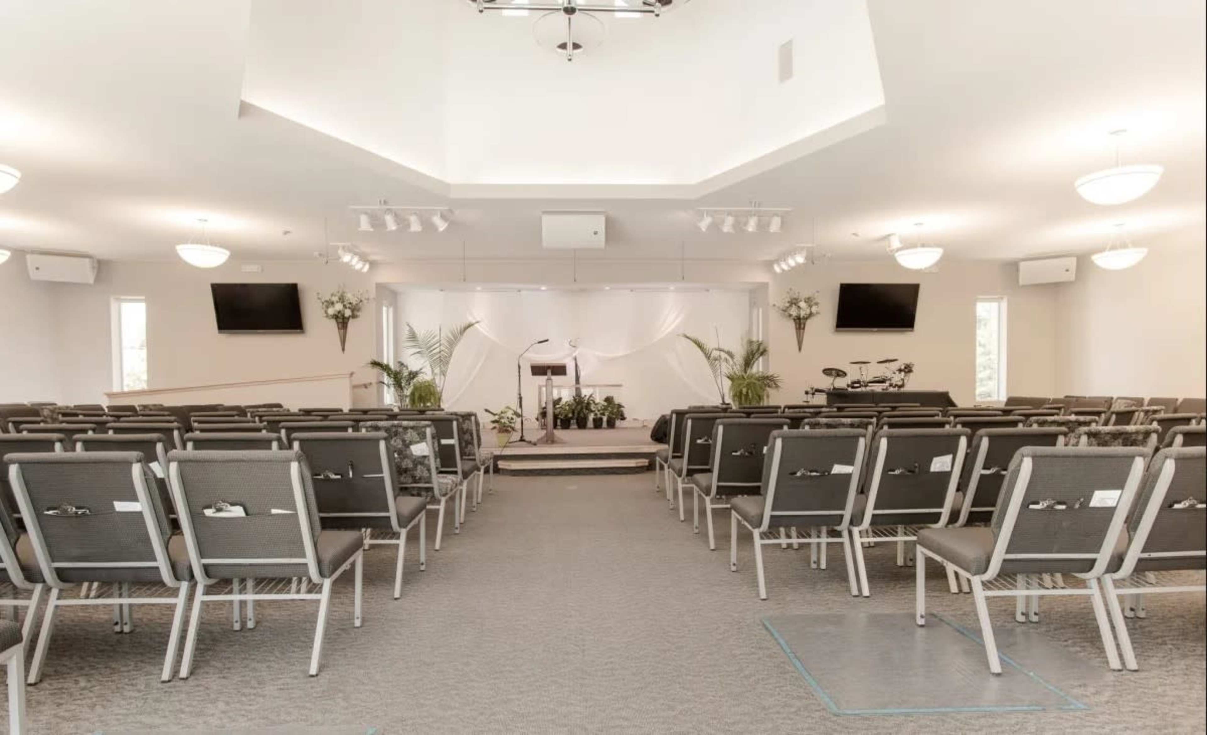 A well-lit, empty event space with rows of chairs facing a stage decorated with plants and a podium.