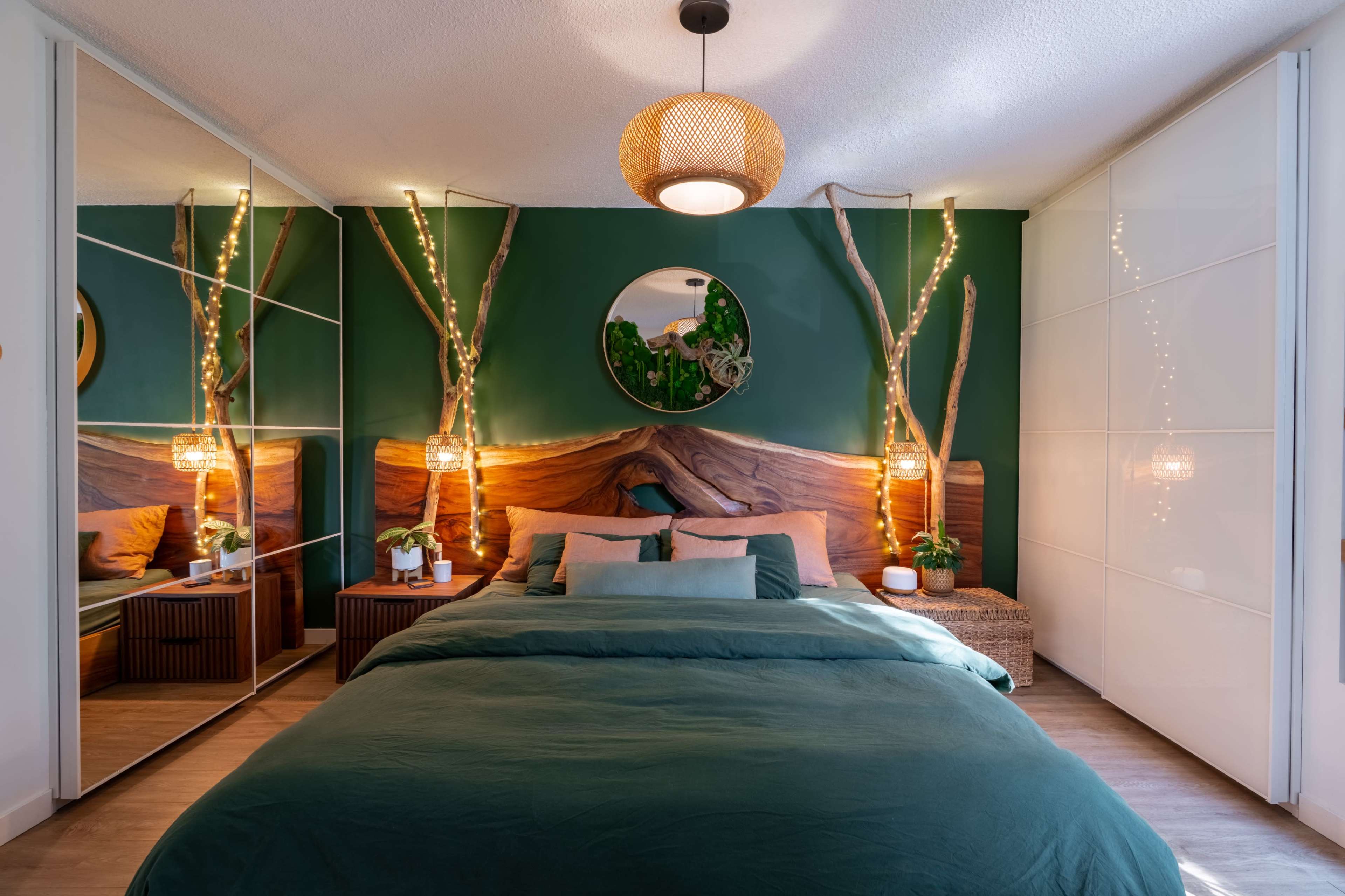 The image shows a modern bedroom with a large bed dressed in green bedding, accented by wooden features and fairy lights on the walls.