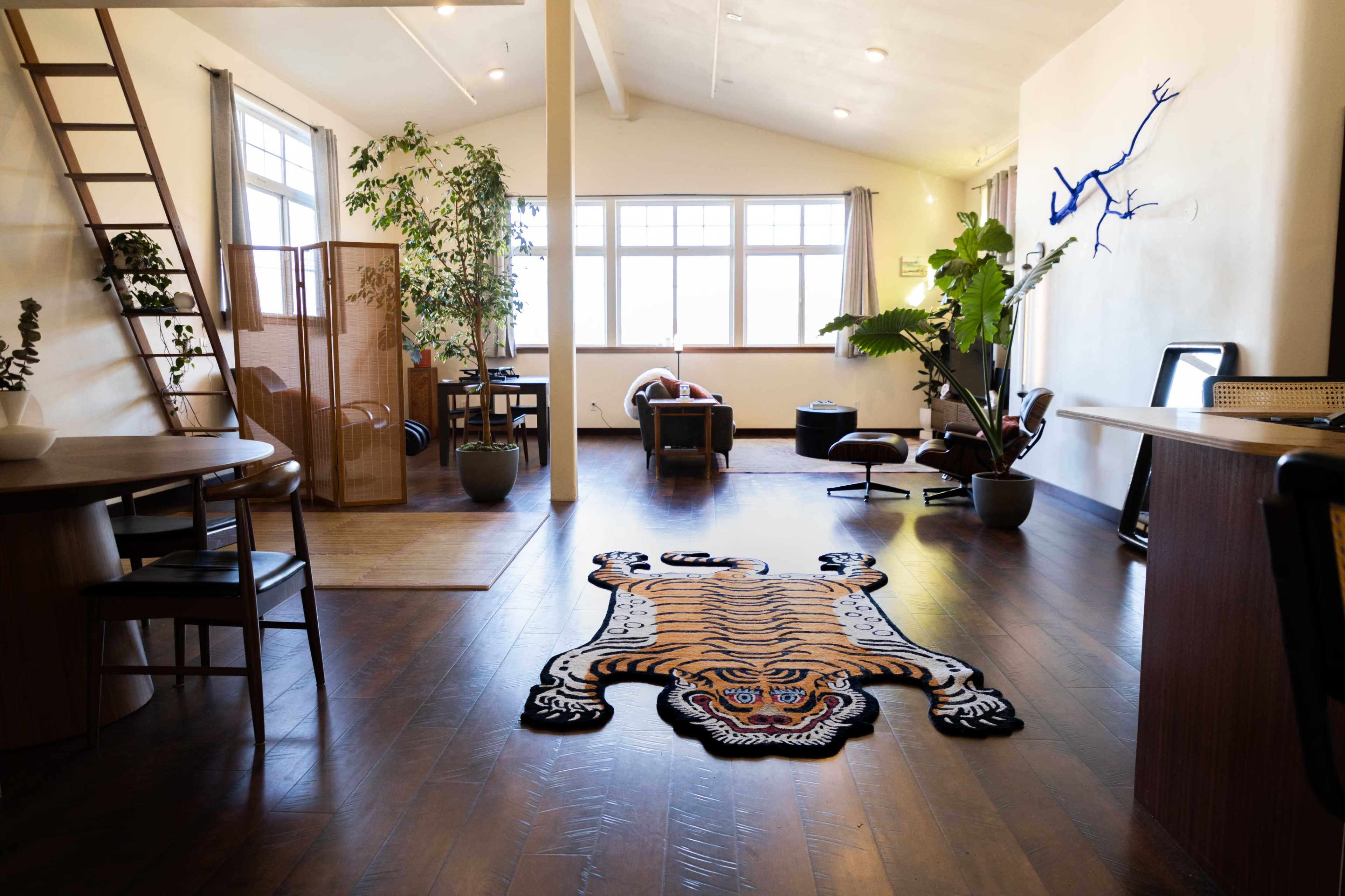 A spacious, modern living area features a distinctive tiger-shaped rug on the polished wooden floor, surrounded by plants and minimalist furnishings.