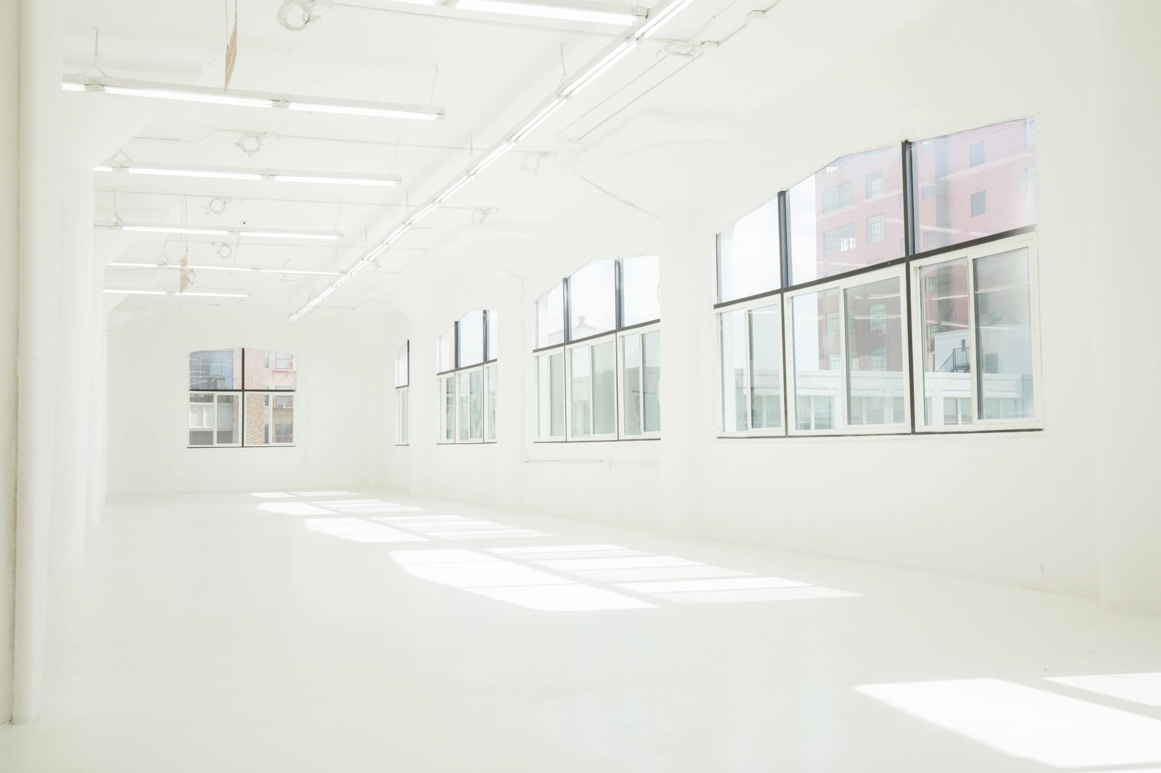 A spacious, well-lit room with large windows and a white floor.