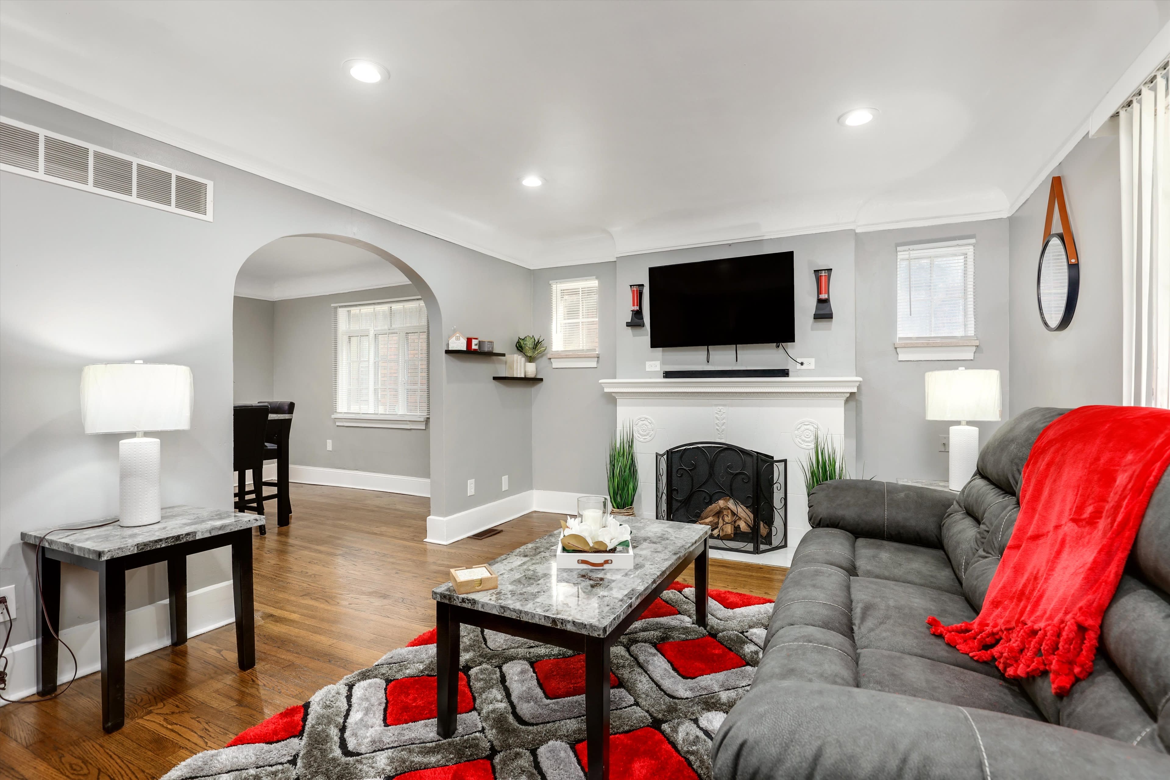 The living room features a gray sofa with a red throw blanket, a marble-topped coffee table, and a wall-mounted television above a fireplace.