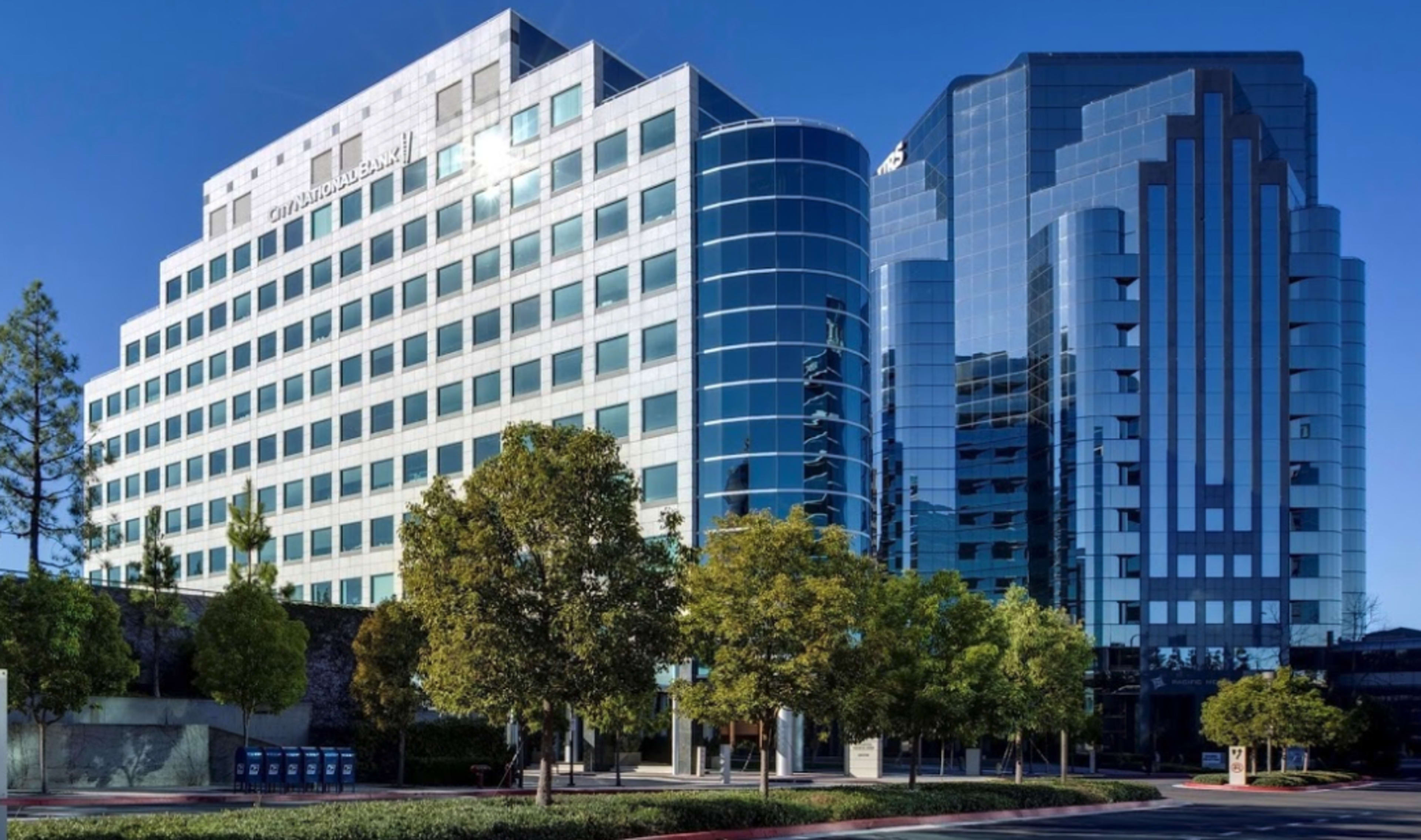 Two modern office buildings with glass facades and landscaped greenery in the foreground.