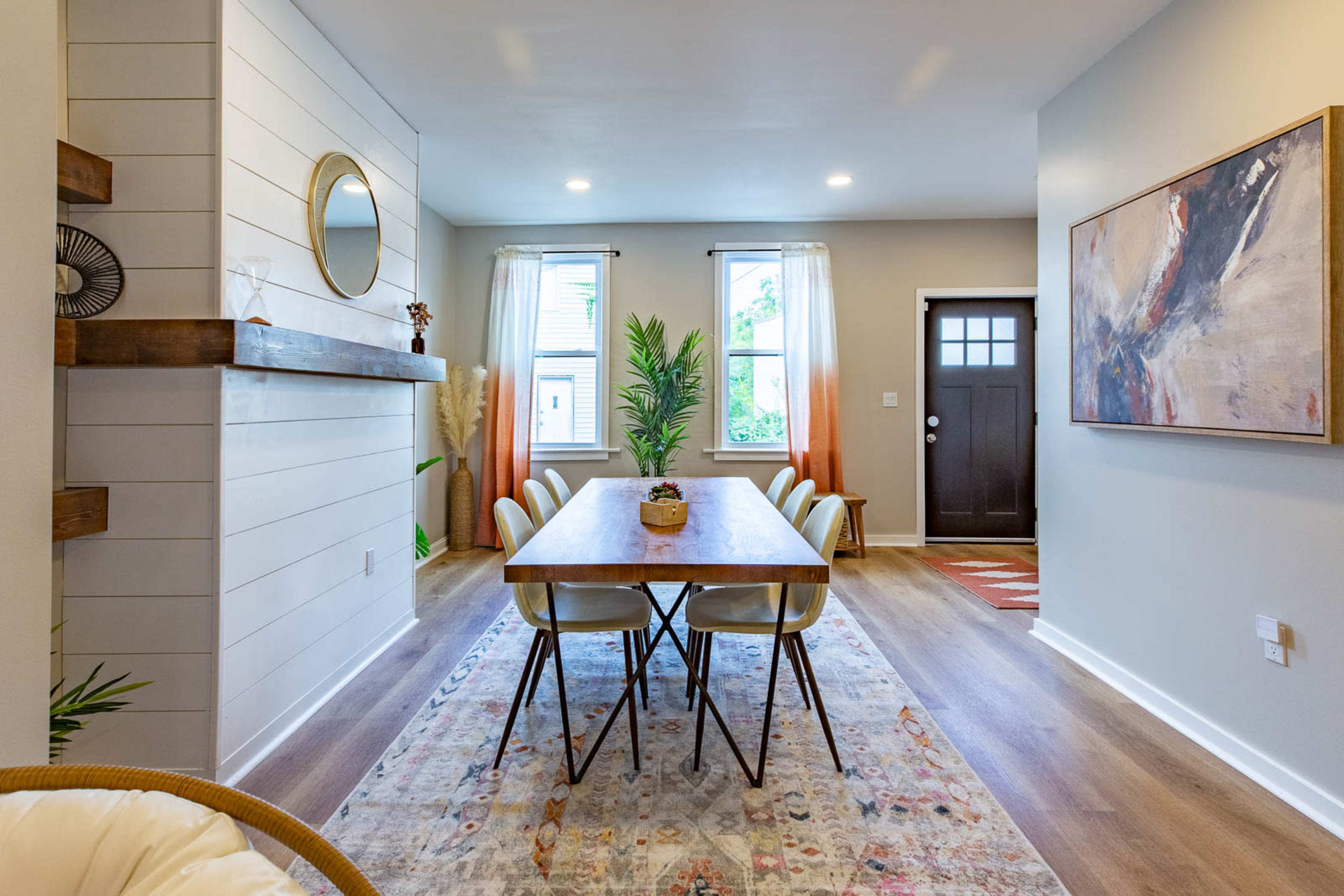 A modern dining area with a wooden table surrounded by chairs, a decorative rug on the floor, and a plant near a window.