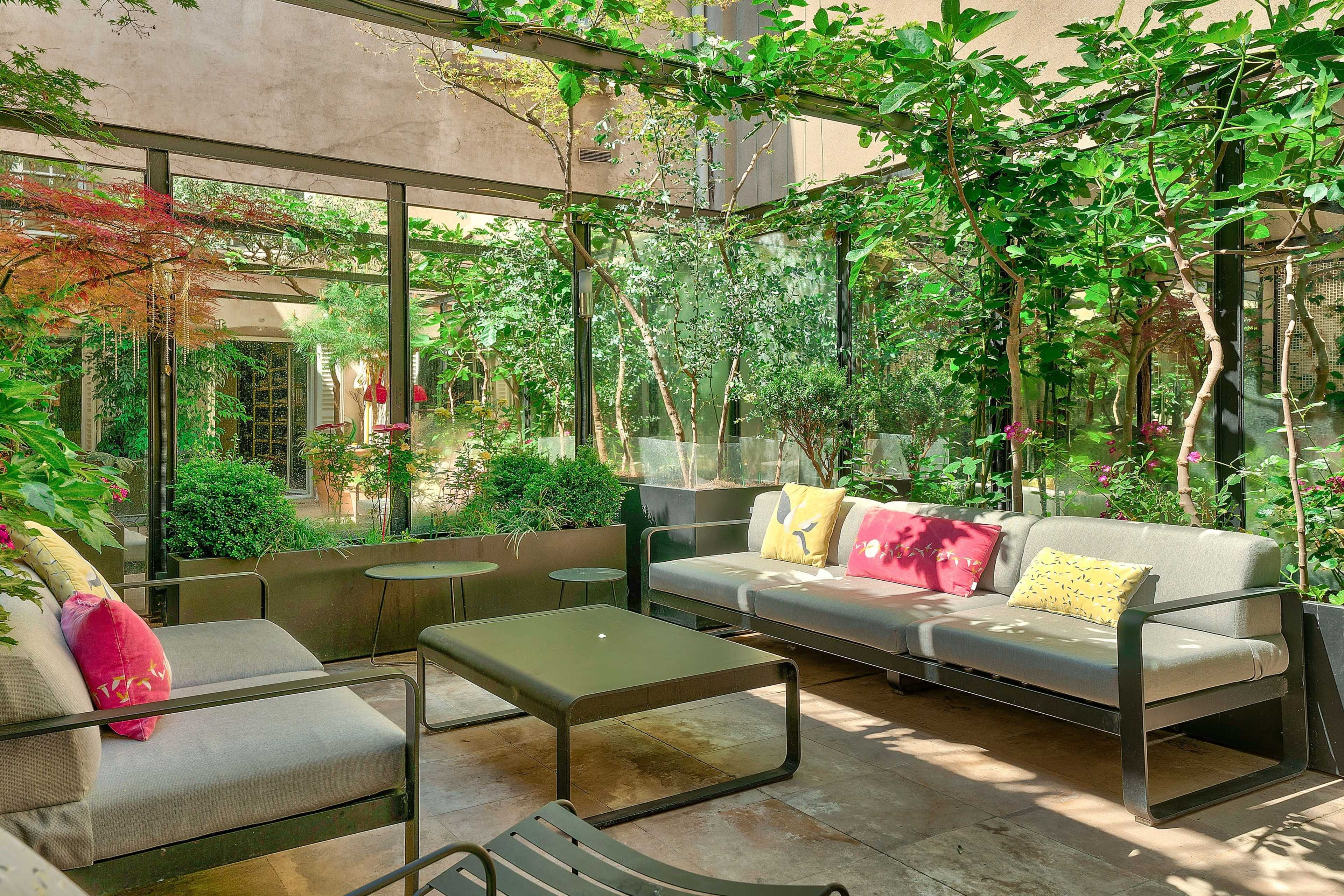 The image features a sunlit glass-enclosed patio adorned with greenery and comfortable seating, creating a serene outdoor atmosphere.