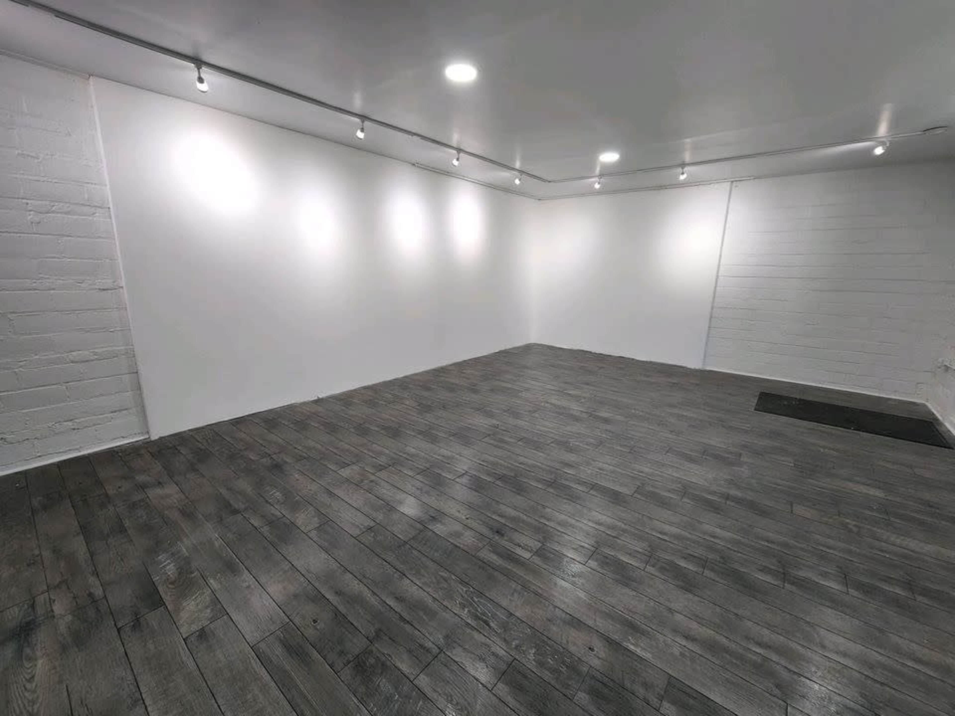 An empty room with a wooden floor and white walls illuminated by overhead track lighting.