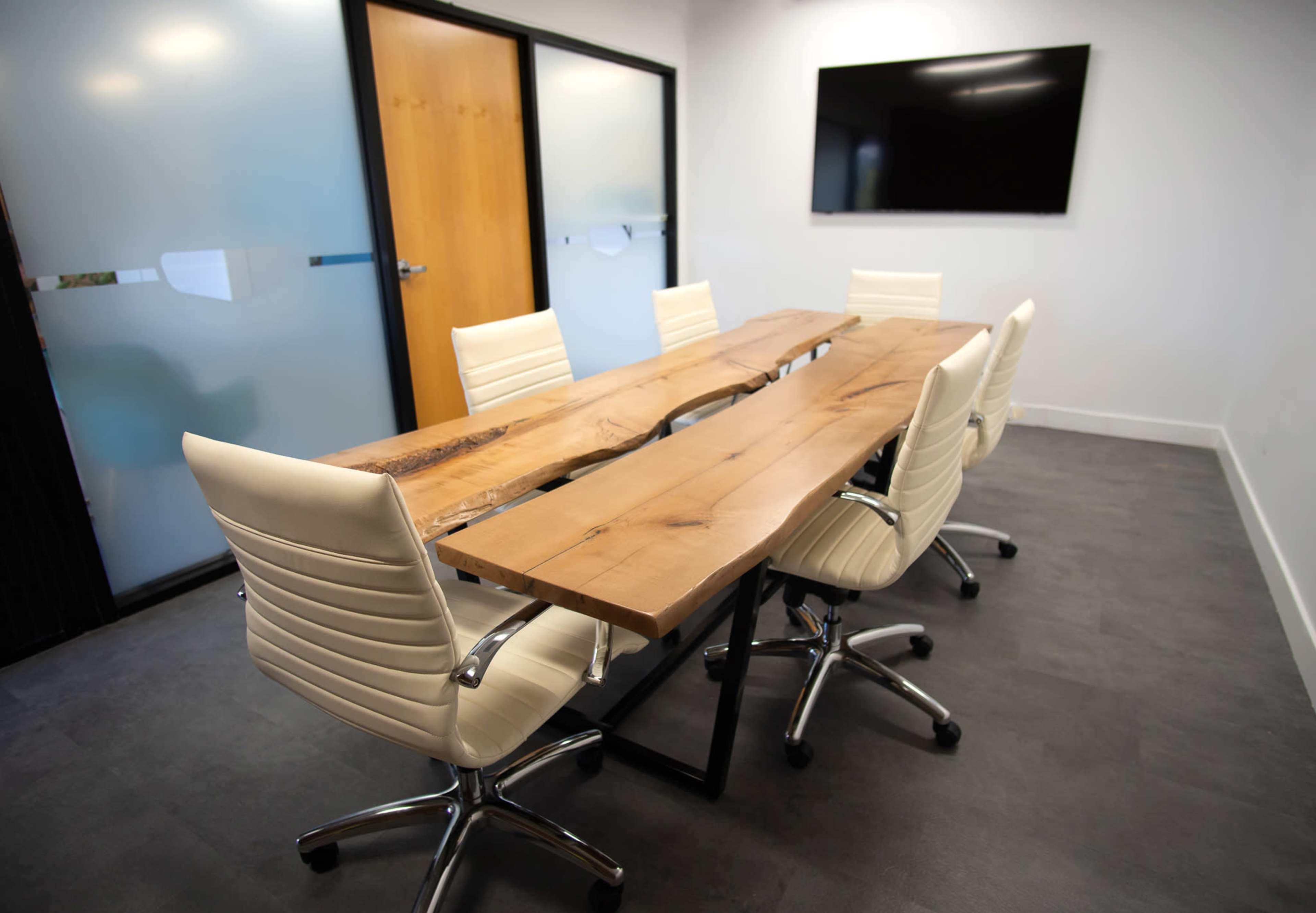 A modern conference room features a long wooden table with a unique design and six white swivel chairs.