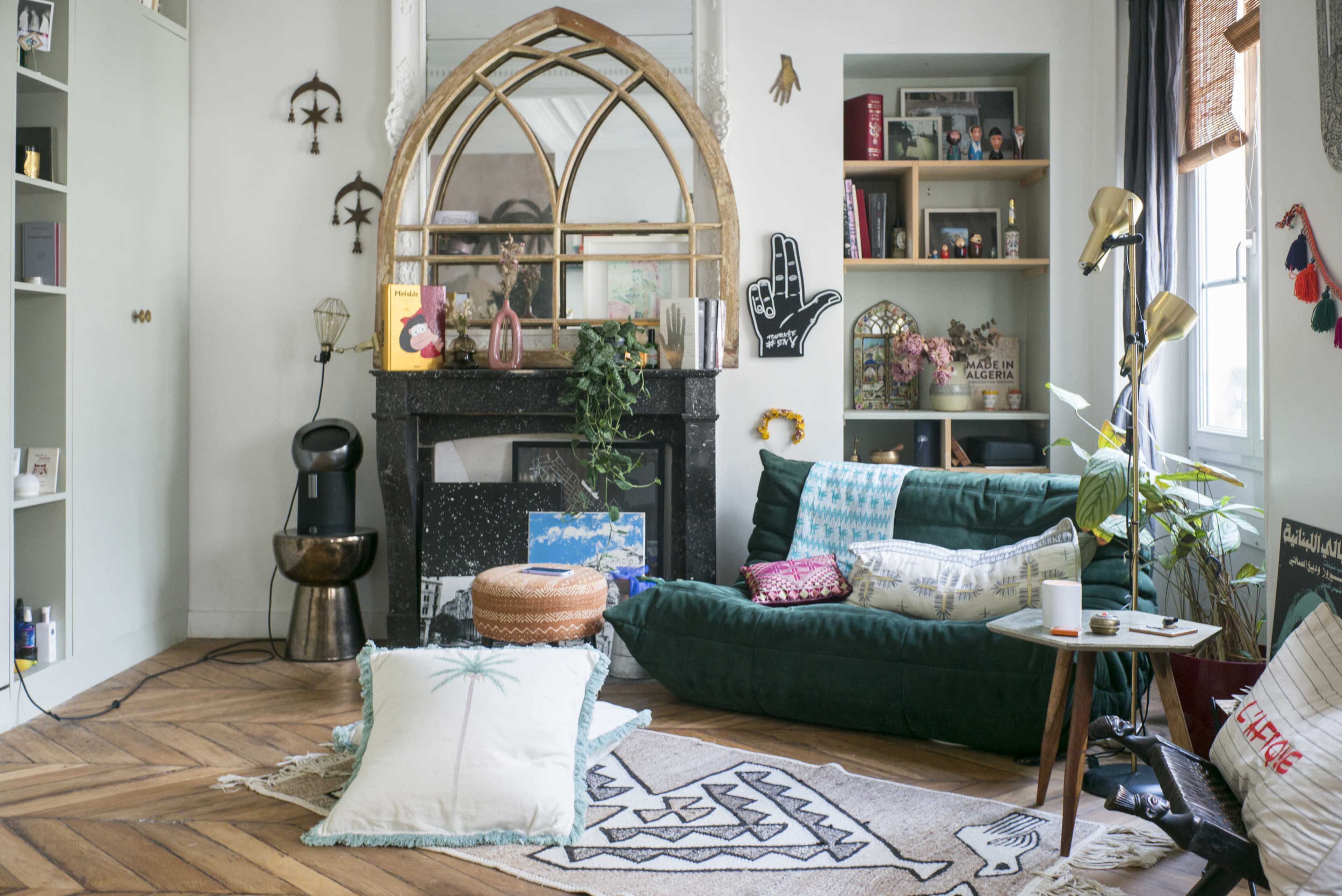 A cozy living room with a green sofa, a patterned rug, and decorative items arranged around a fireplace and bookshelf.