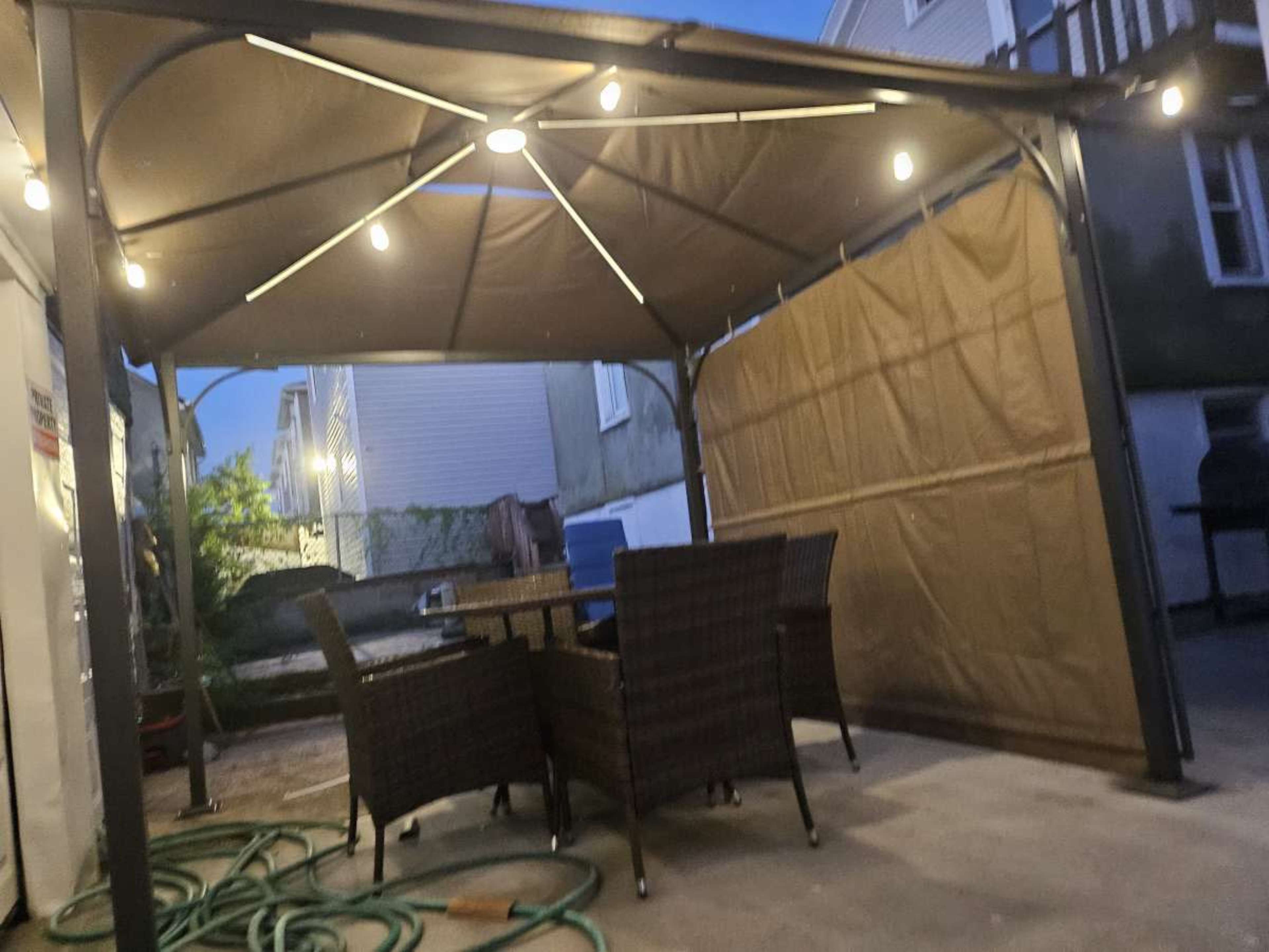 A patio area with a gazebo featuring lights and a set of four wicker chairs around a rectangular table.