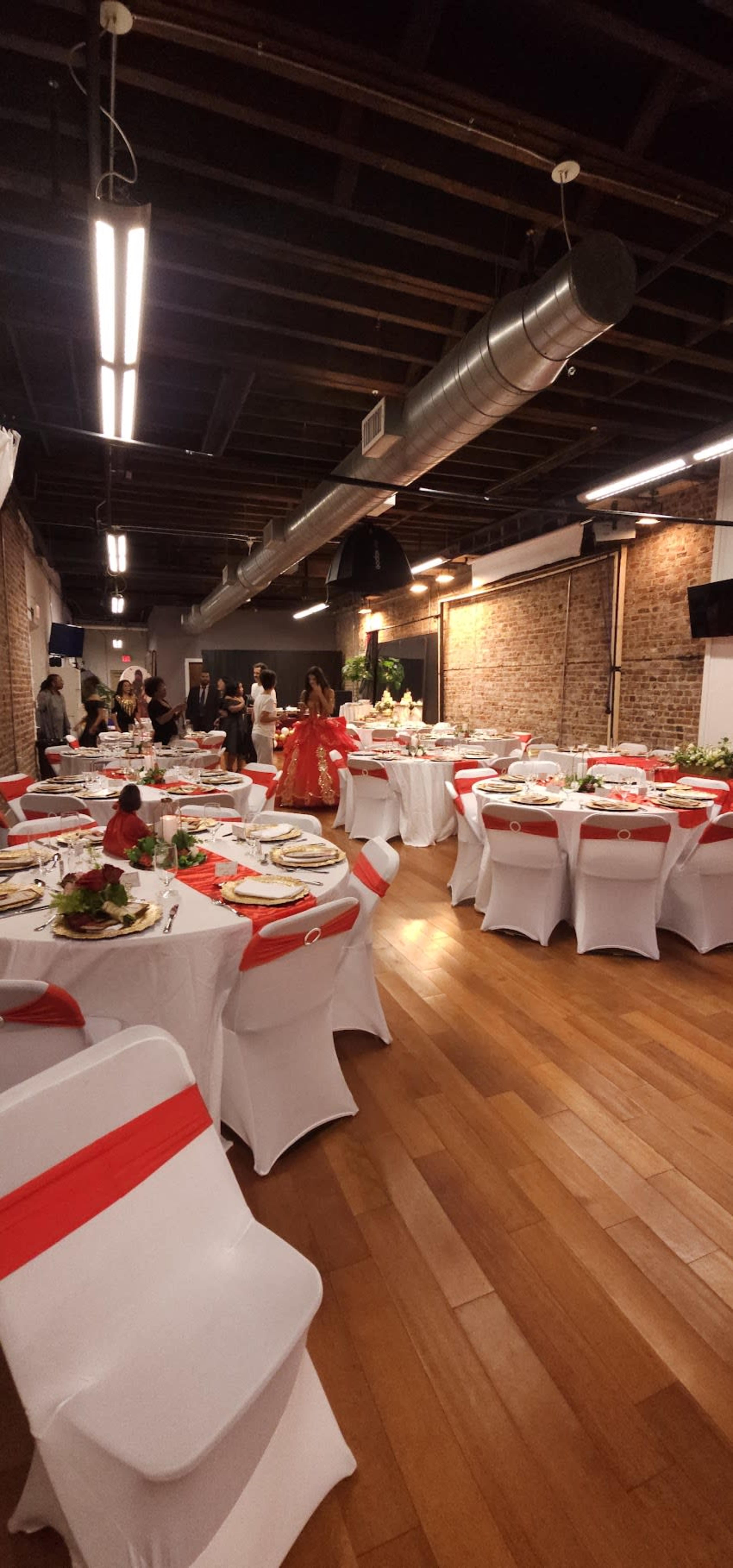 A banquet hall is set up for an event with white tables adorned with red accents and floral centerpieces.