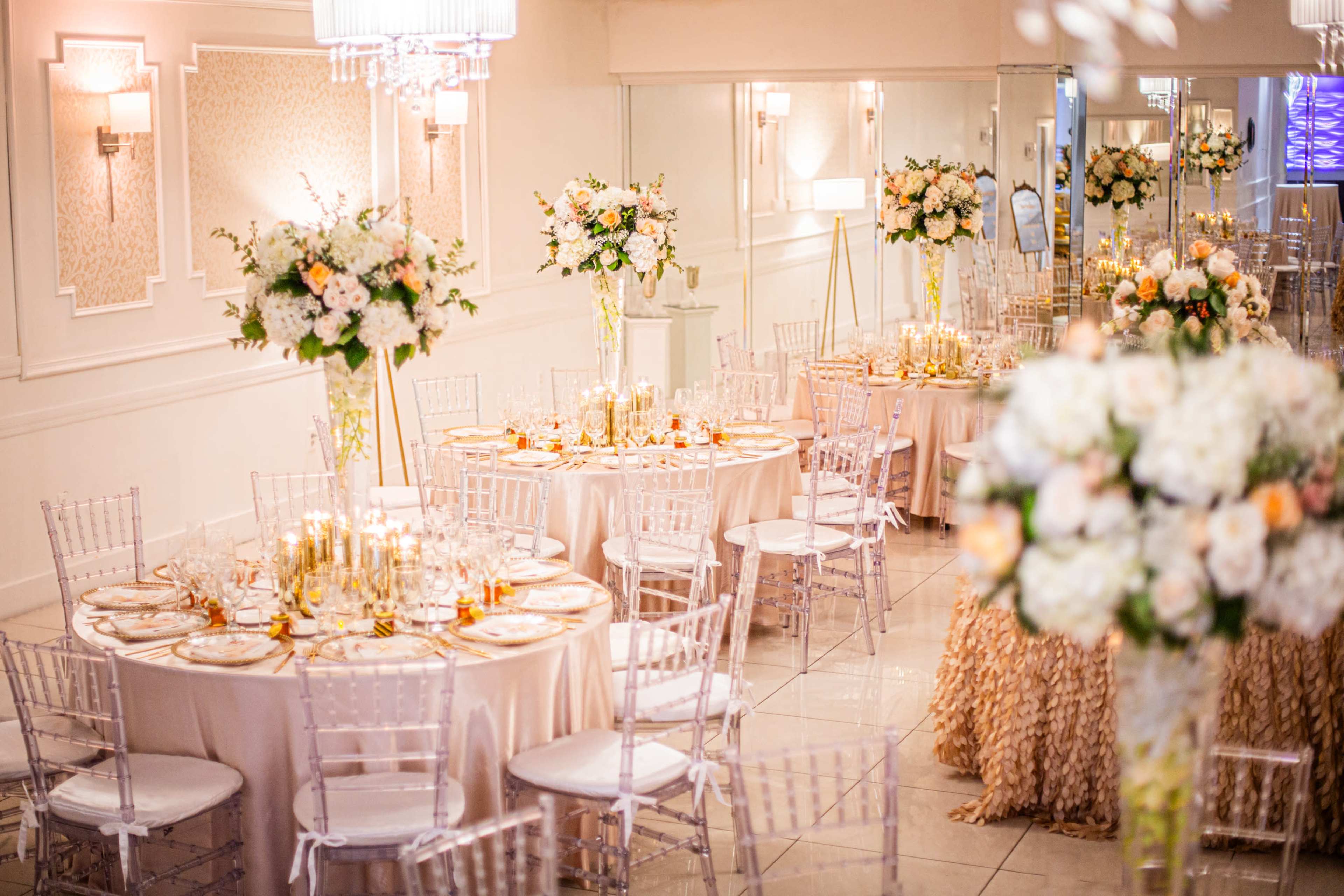 The image shows an elegantly decorated banquet hall with round tables adorned with floral centerpieces and candlelight, set for an event.