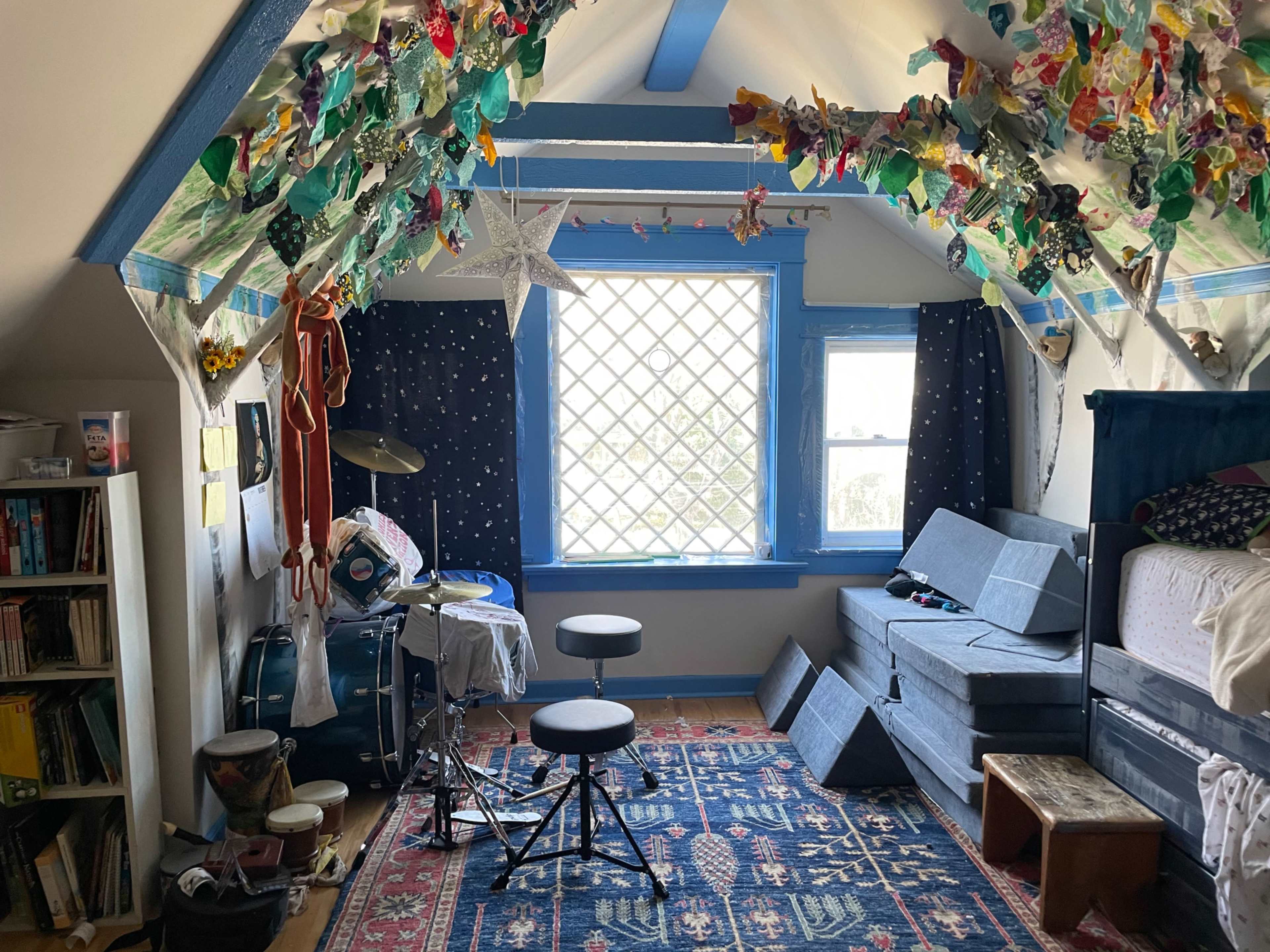 The image shows a cozy, sloped-ceiling room with musical instruments, a bed, and colorful decorations overhead.