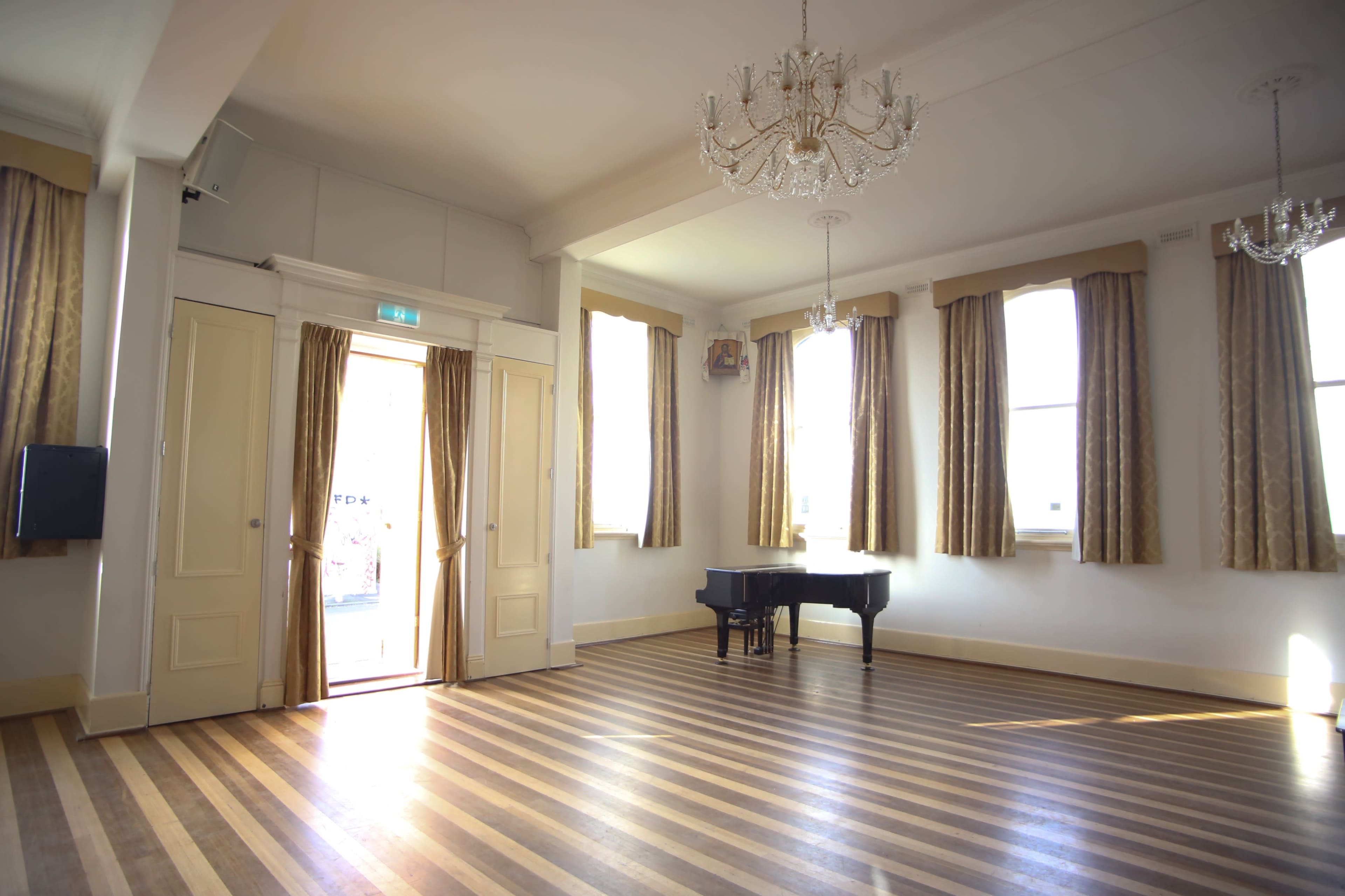 A spacious room with a grand piano, wooden striped flooring, and tall windows dressed with curtains.