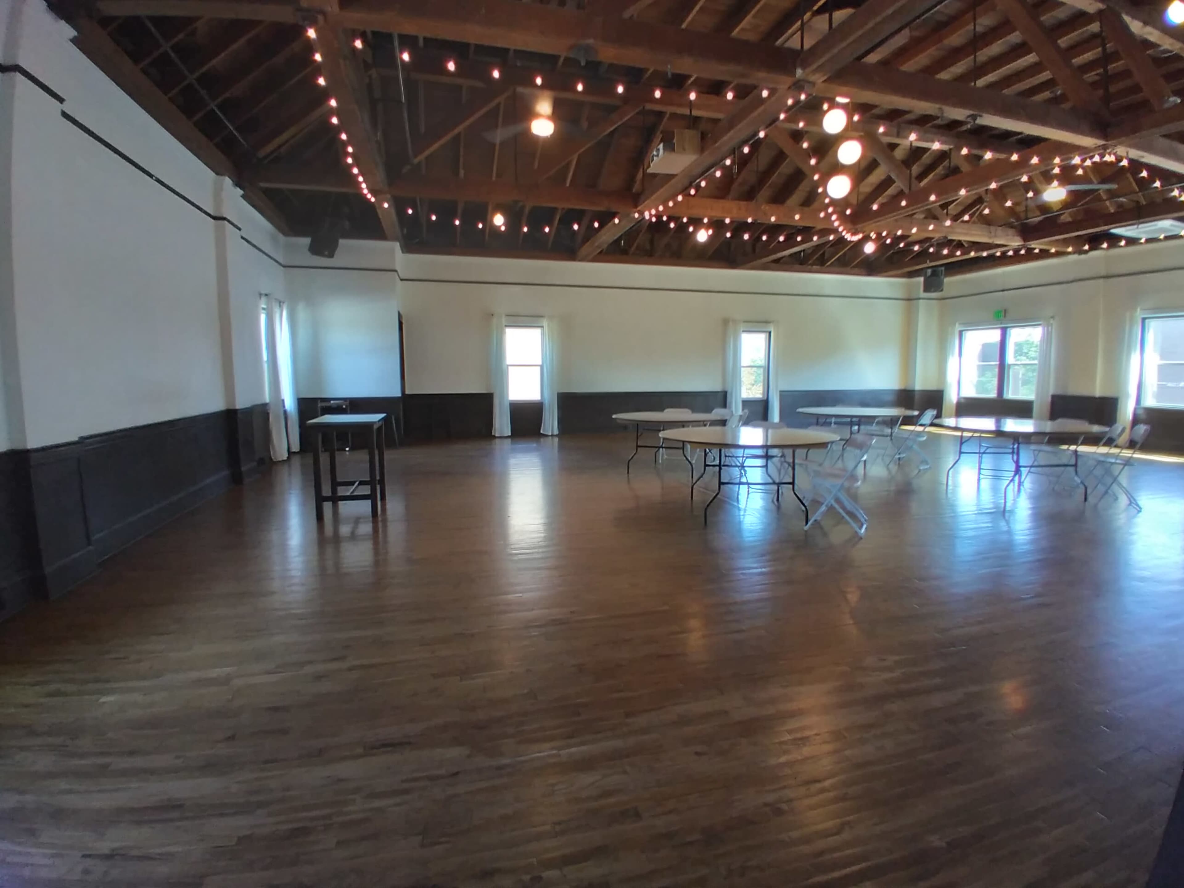A spacious wooden venue with string lights and several folding tables arranged throughout the room.