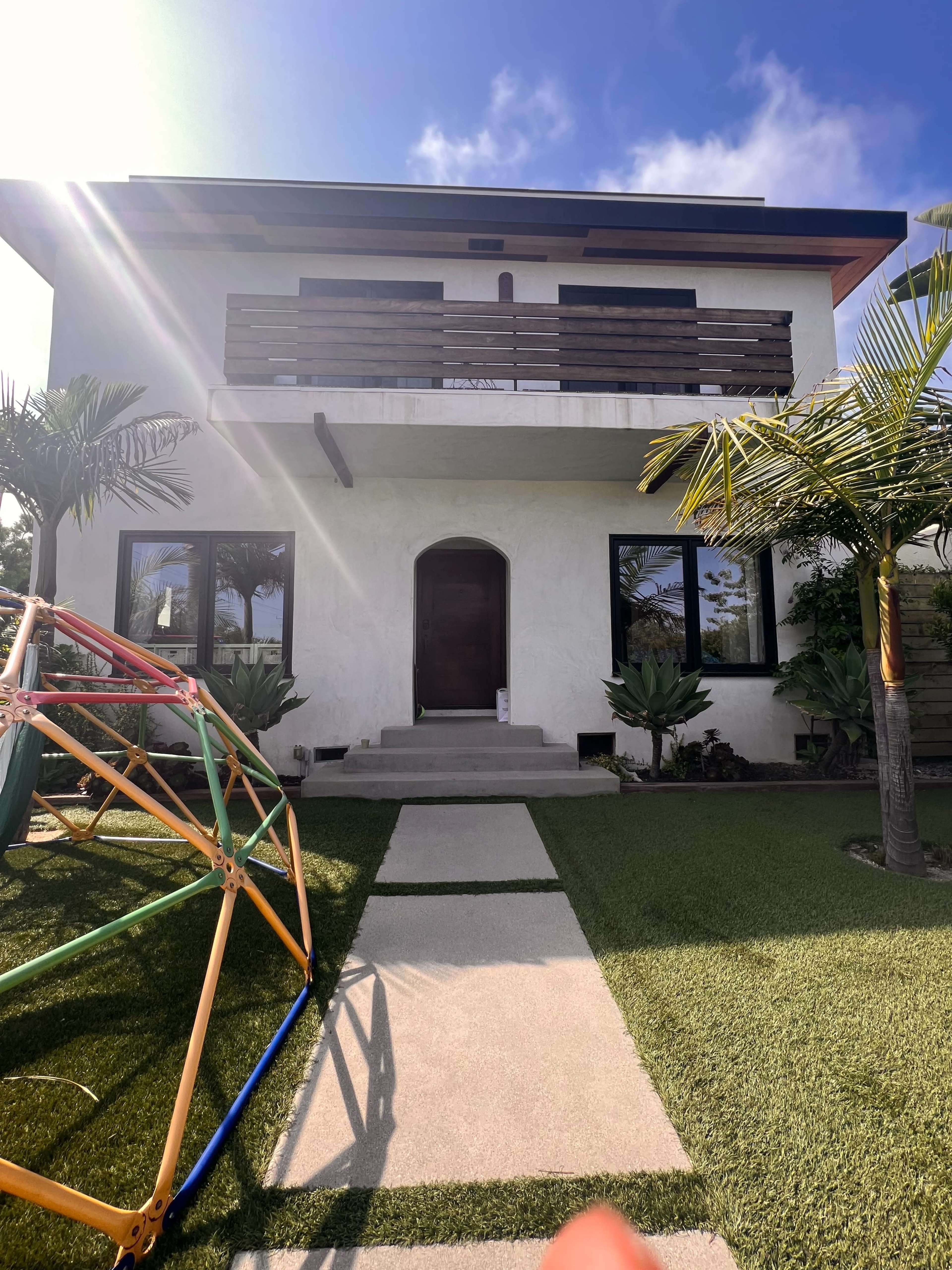 A two-story house with a modern design, featuring a stepped pathway leading to the entrance and a colorful play structure in the foreground.