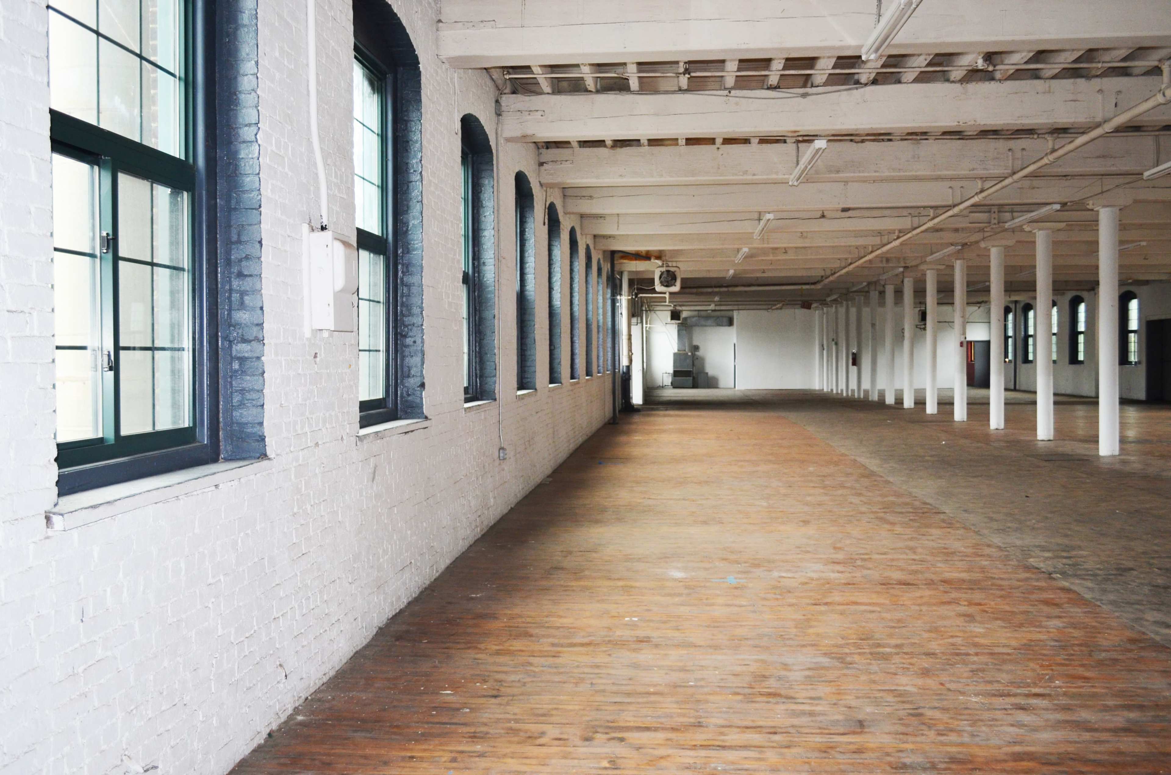A spacious, empty interior of a building with large windows and wooden floors.