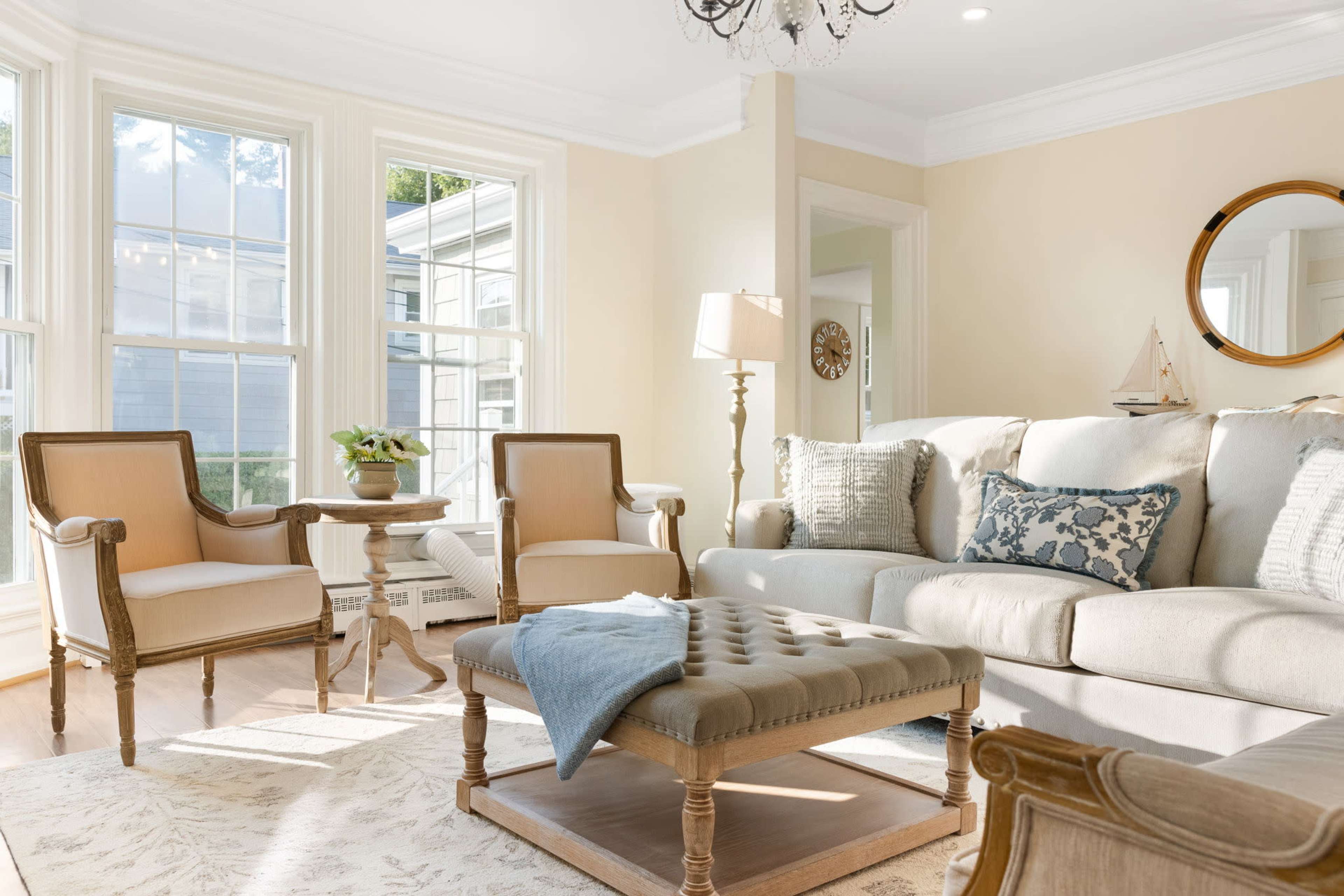 A bright living room featuring two upholstered chairs, a coffee table, a light-colored sofa, and large windows that allow natural light to enter the space.