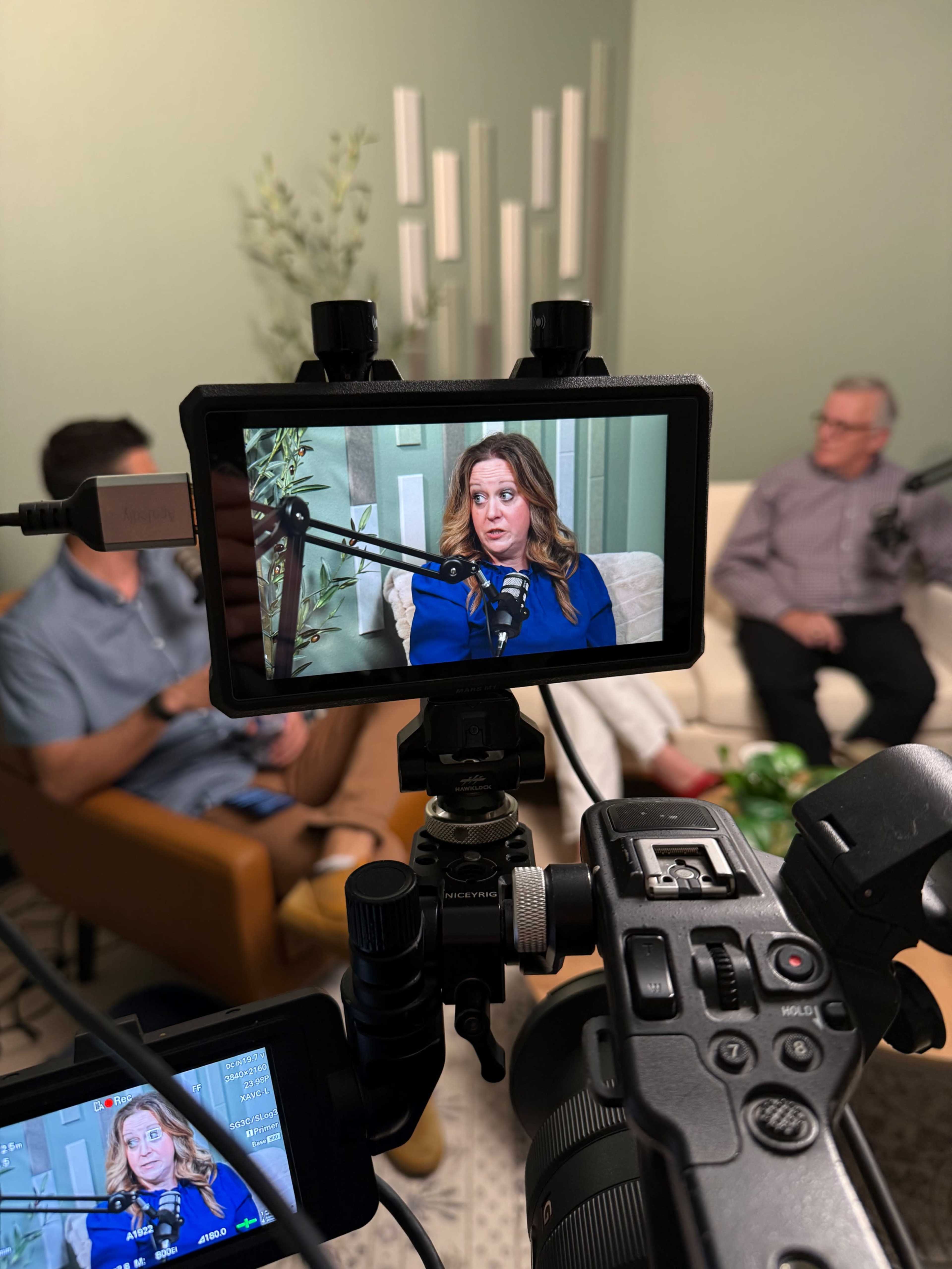 A woman is being interviewed in a studio setup while being filmed by a camera on a tripod.
