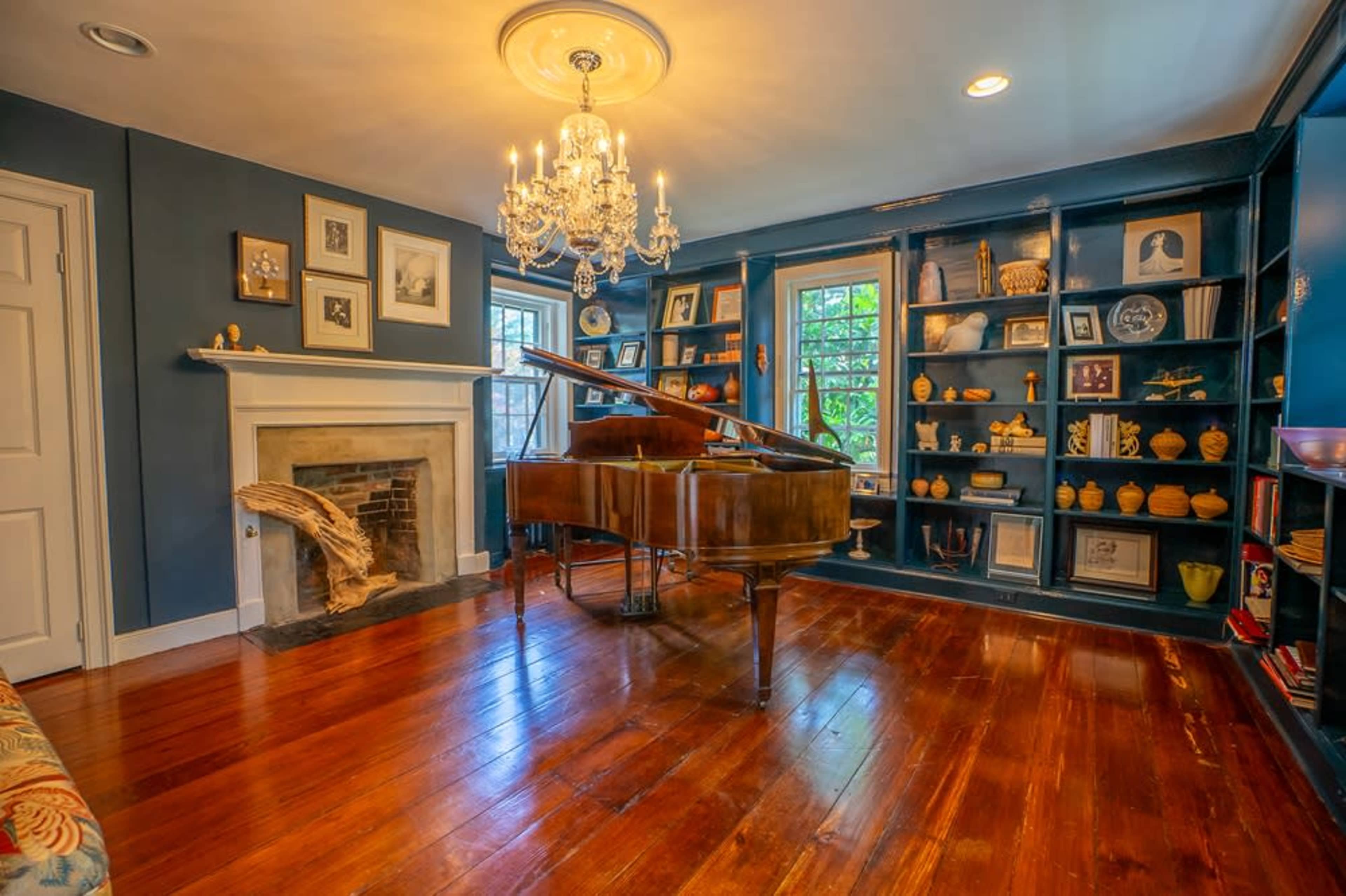 A grand piano is positioned in the center of a room with blue walls, a fireplace, and built-in shelves lined with decorative items.