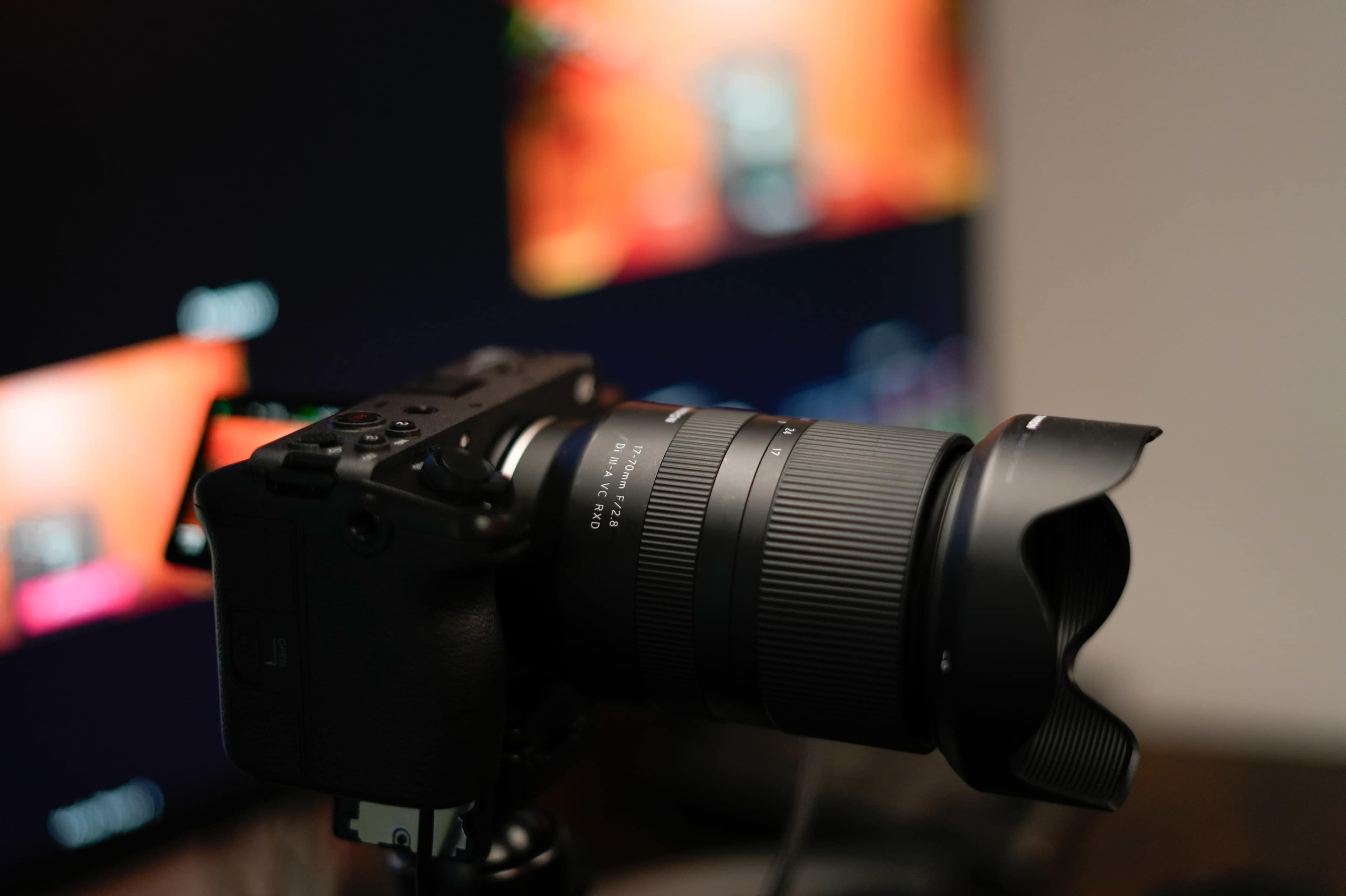A professional camera is positioned on a tripod in front of a blurred computer display featuring colorful images.