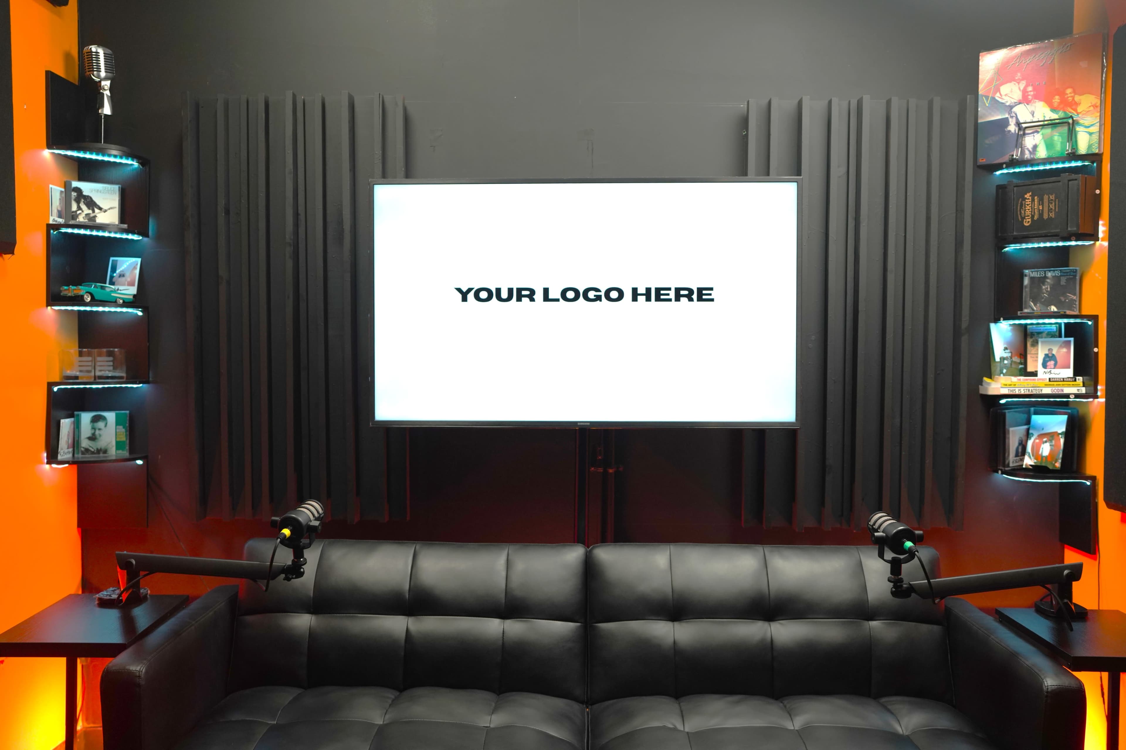 The image shows a modern studio setup featuring a black couch, a large screen displaying the text "YOUR LOGO HERE," and shelves with various items on either side.