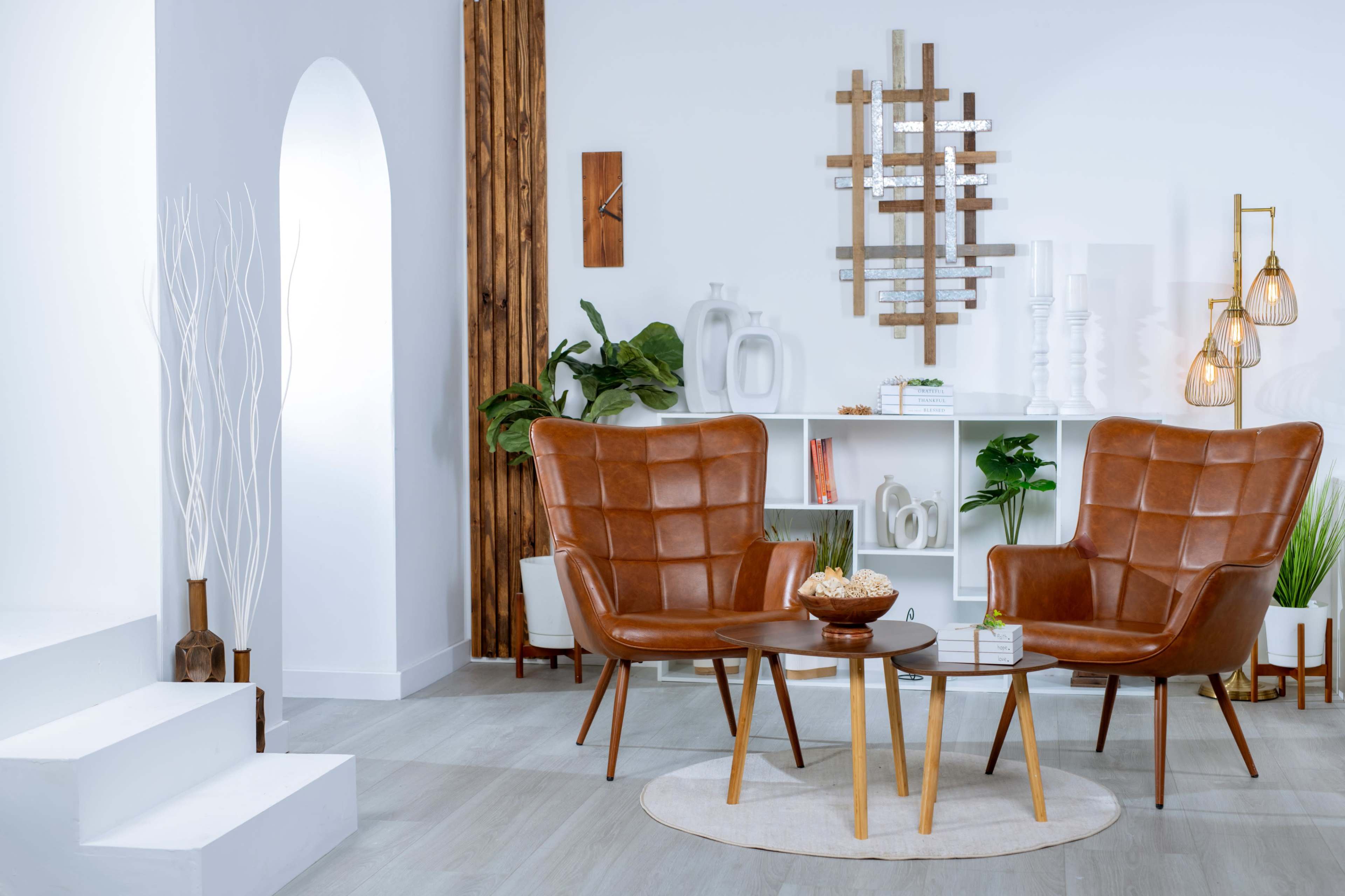 A living room features two brown chairs and a circular table, surrounded by plants and decorative items on a white wall shelf.