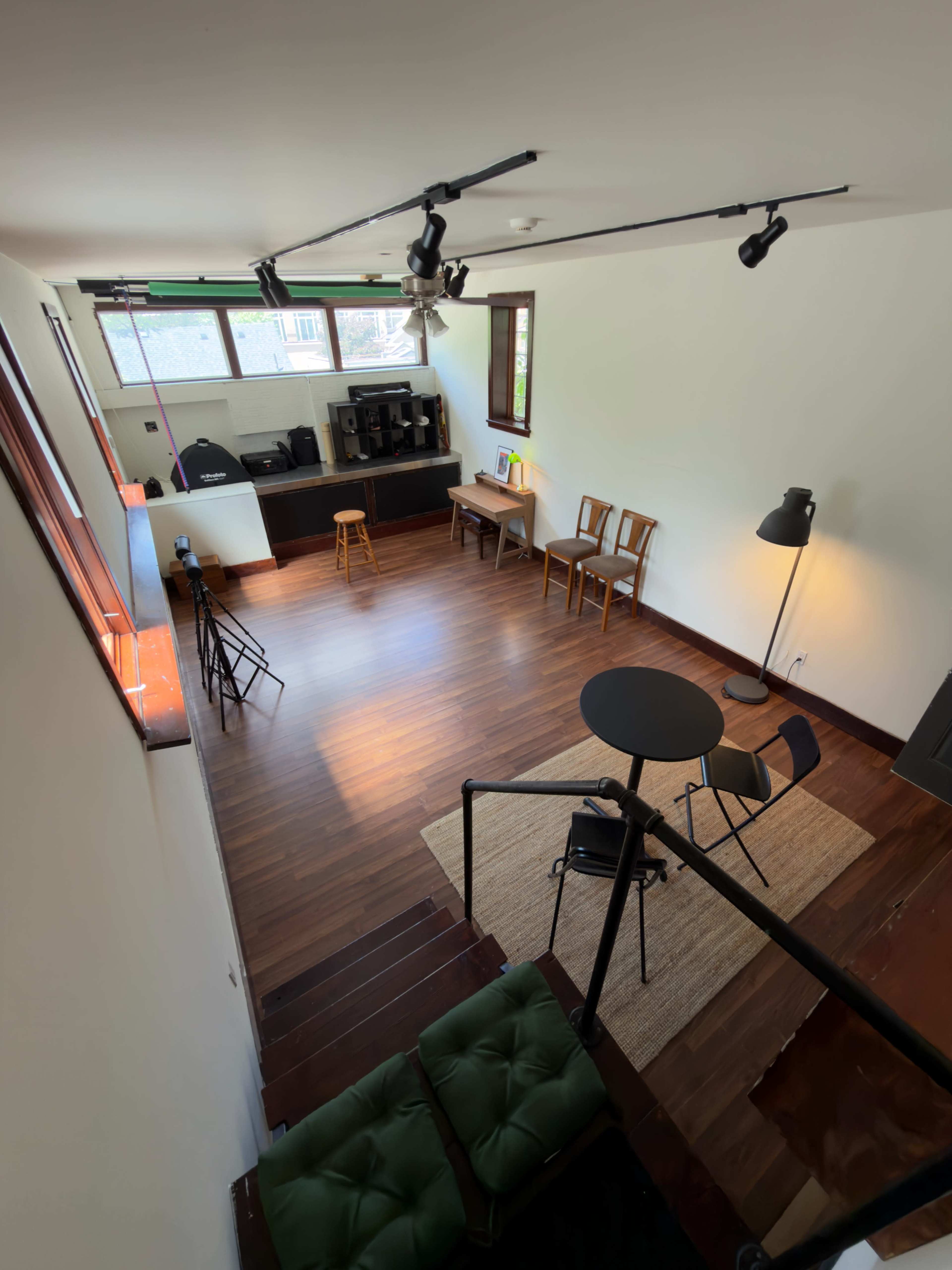 The image shows a spacious, well-lit room with wooden flooring, a table and chairs, and a small kitchenette area.