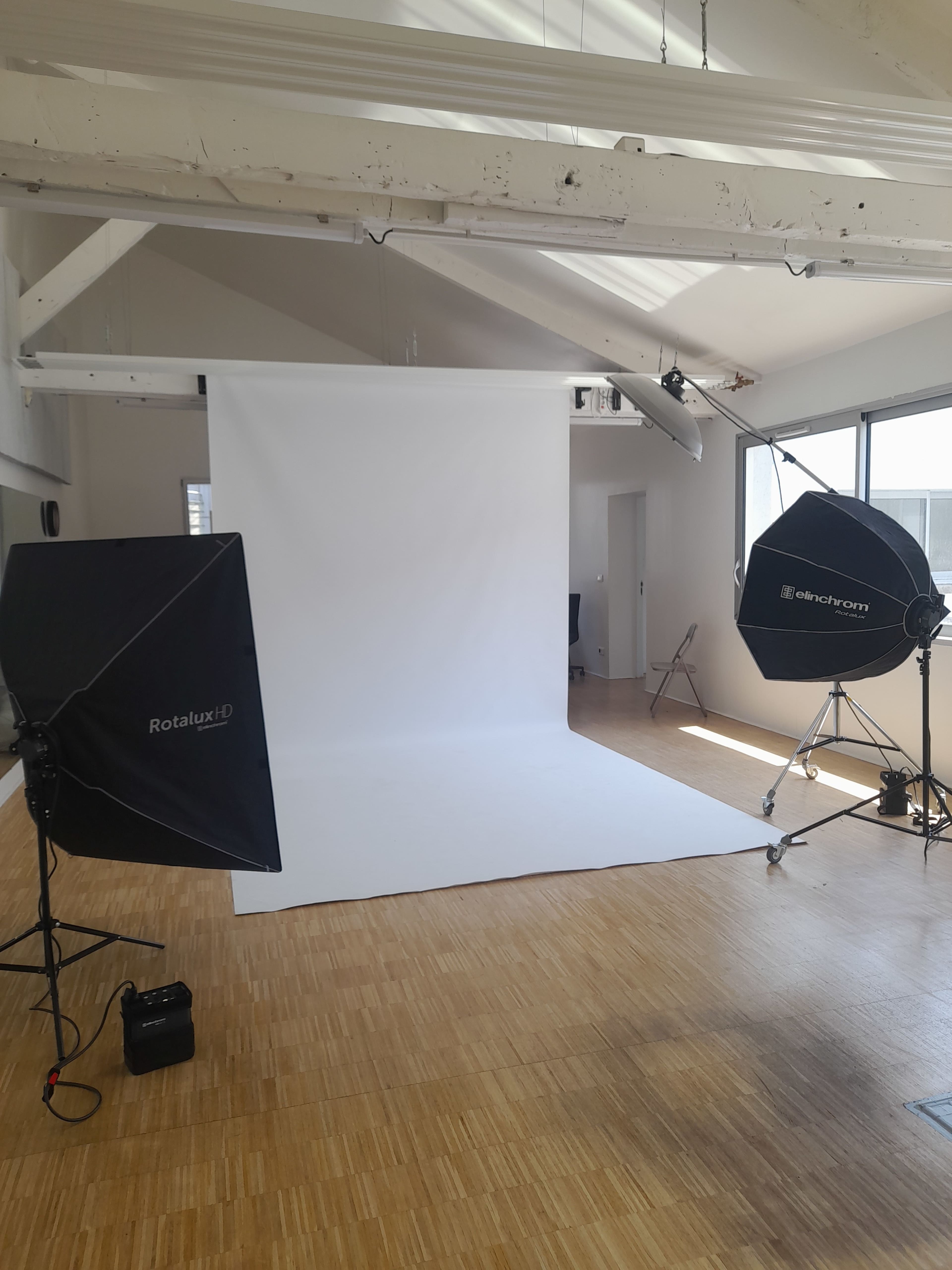 The image shows a photography studio equipped with lighting equipment and a large white backdrop.