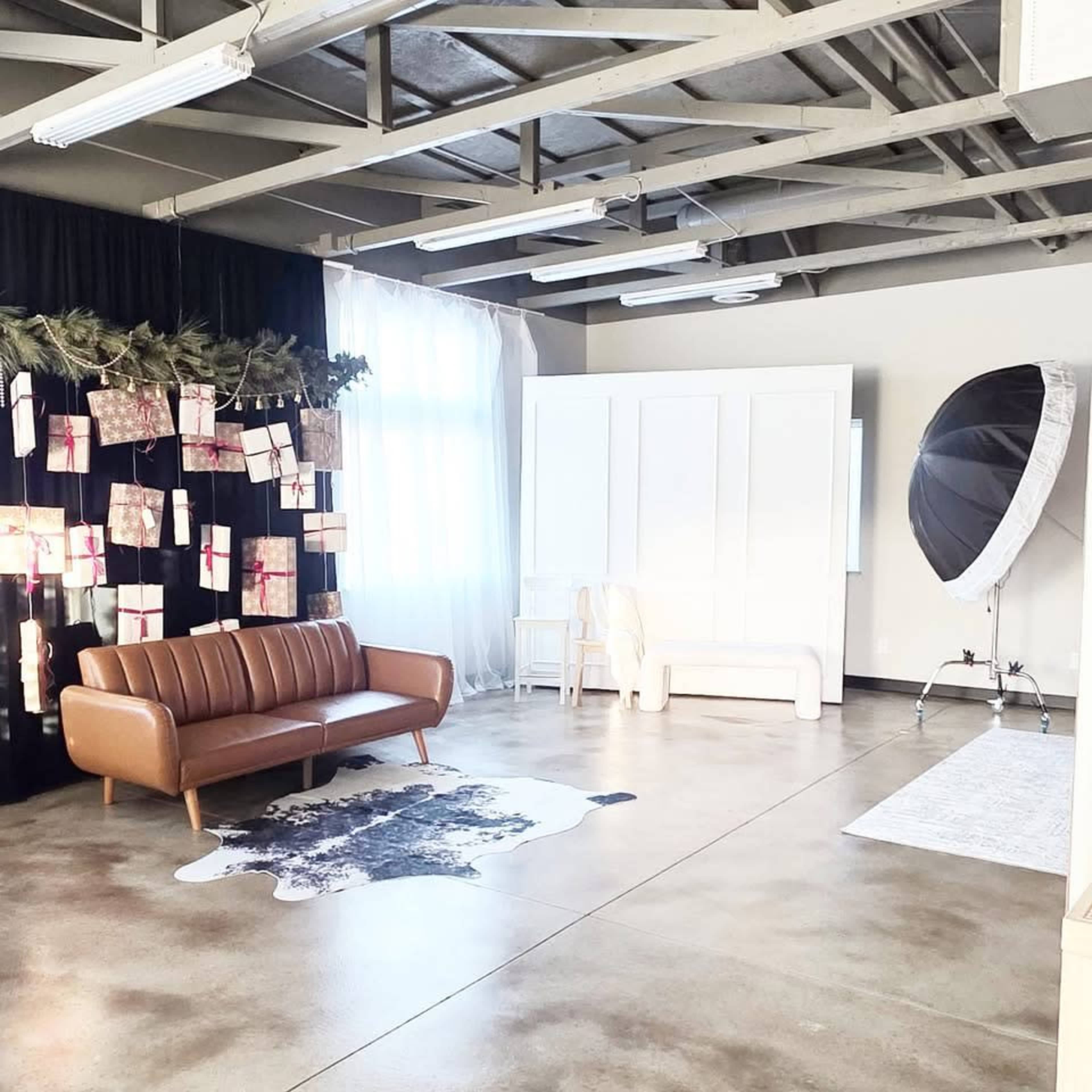 The image shows a spacious studio with a brown leather couch, a large umbrella light, and decorations on the wall made from wrapped gifts.
