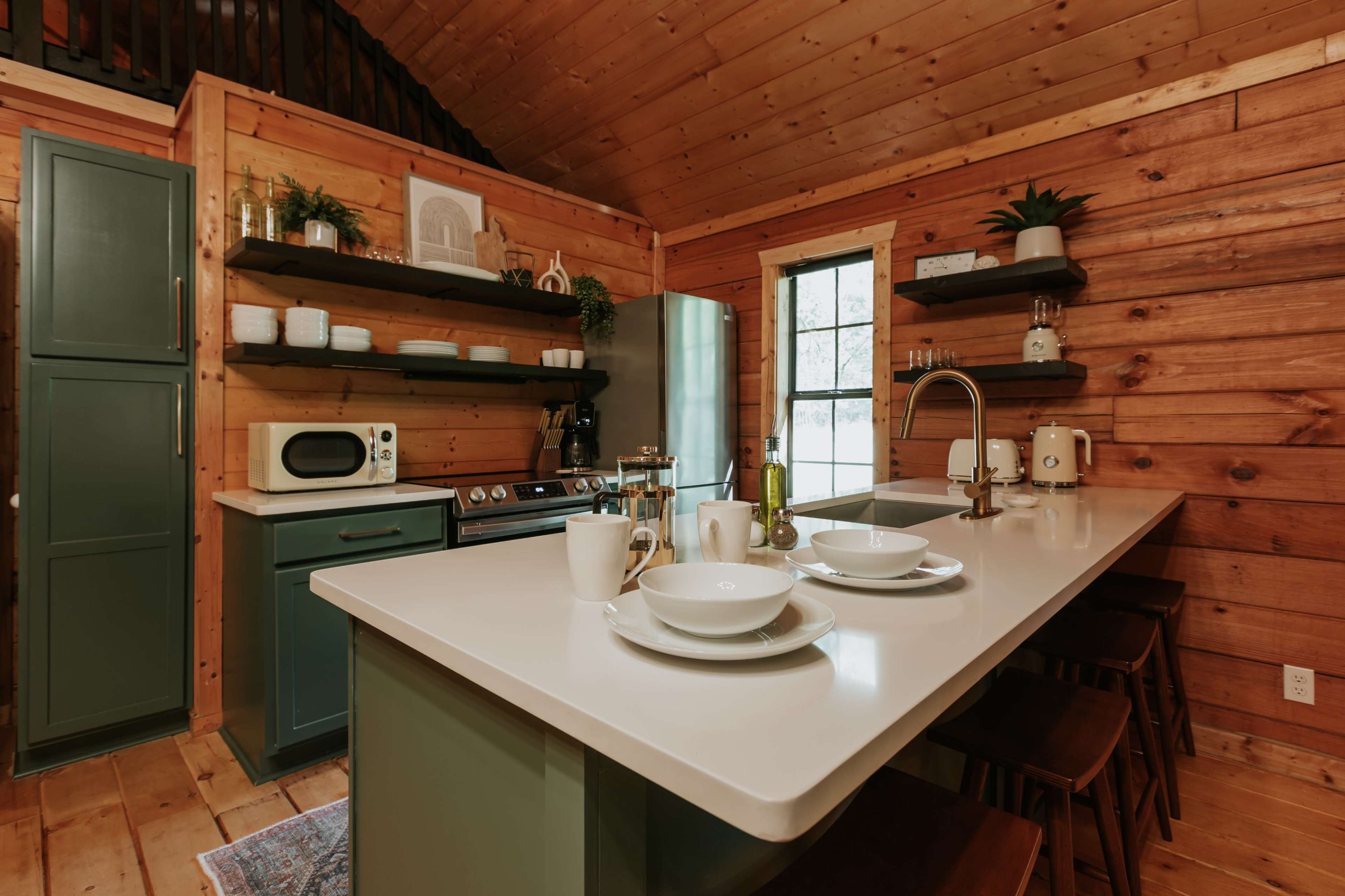 A rustic kitchen with wooden walls, a modern island with tableware, and shelves displaying kitchen items.