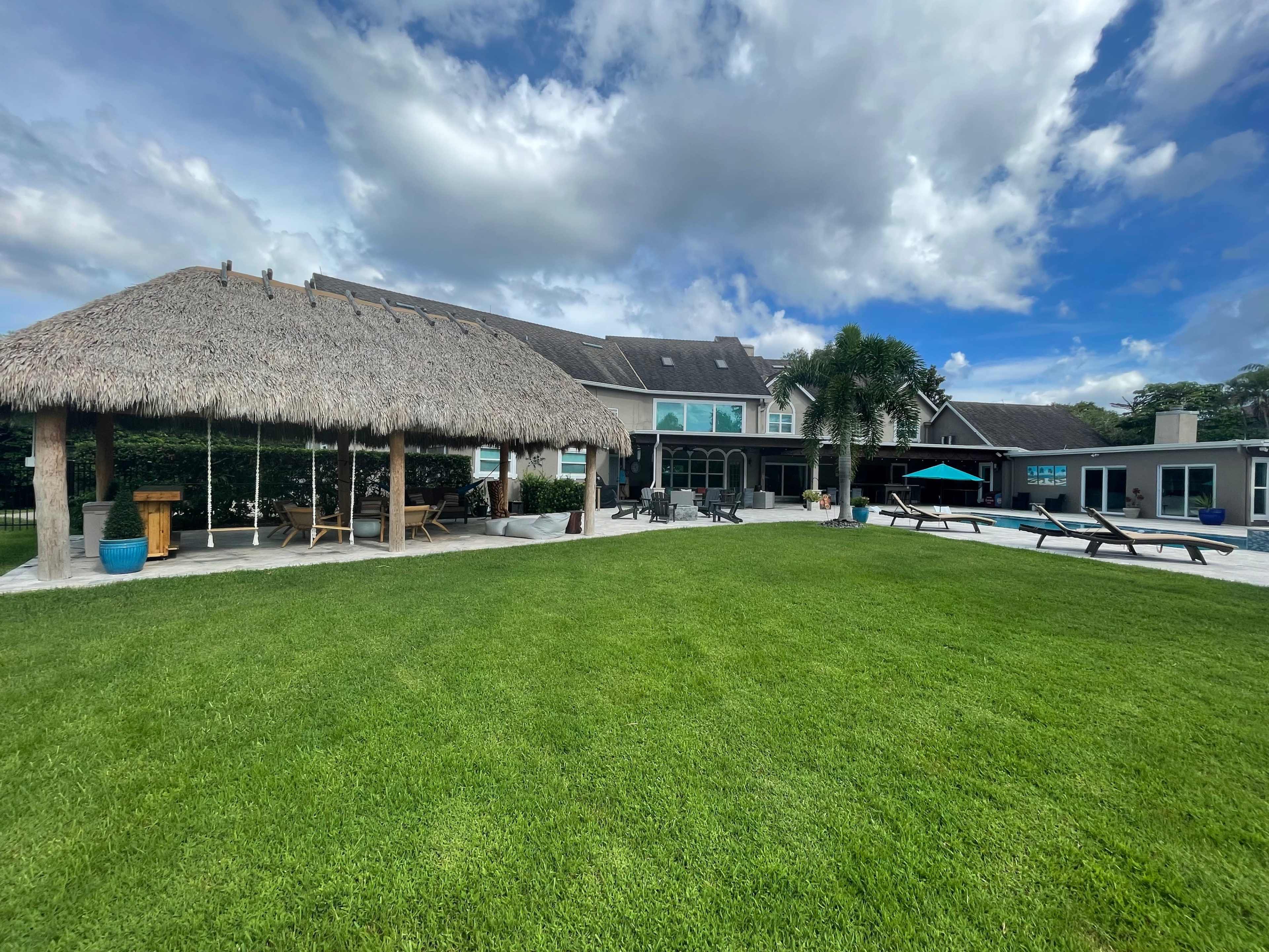 A large grassy area features a thatched-roof gazebo and a spacious building with large windows and outdoor seating.