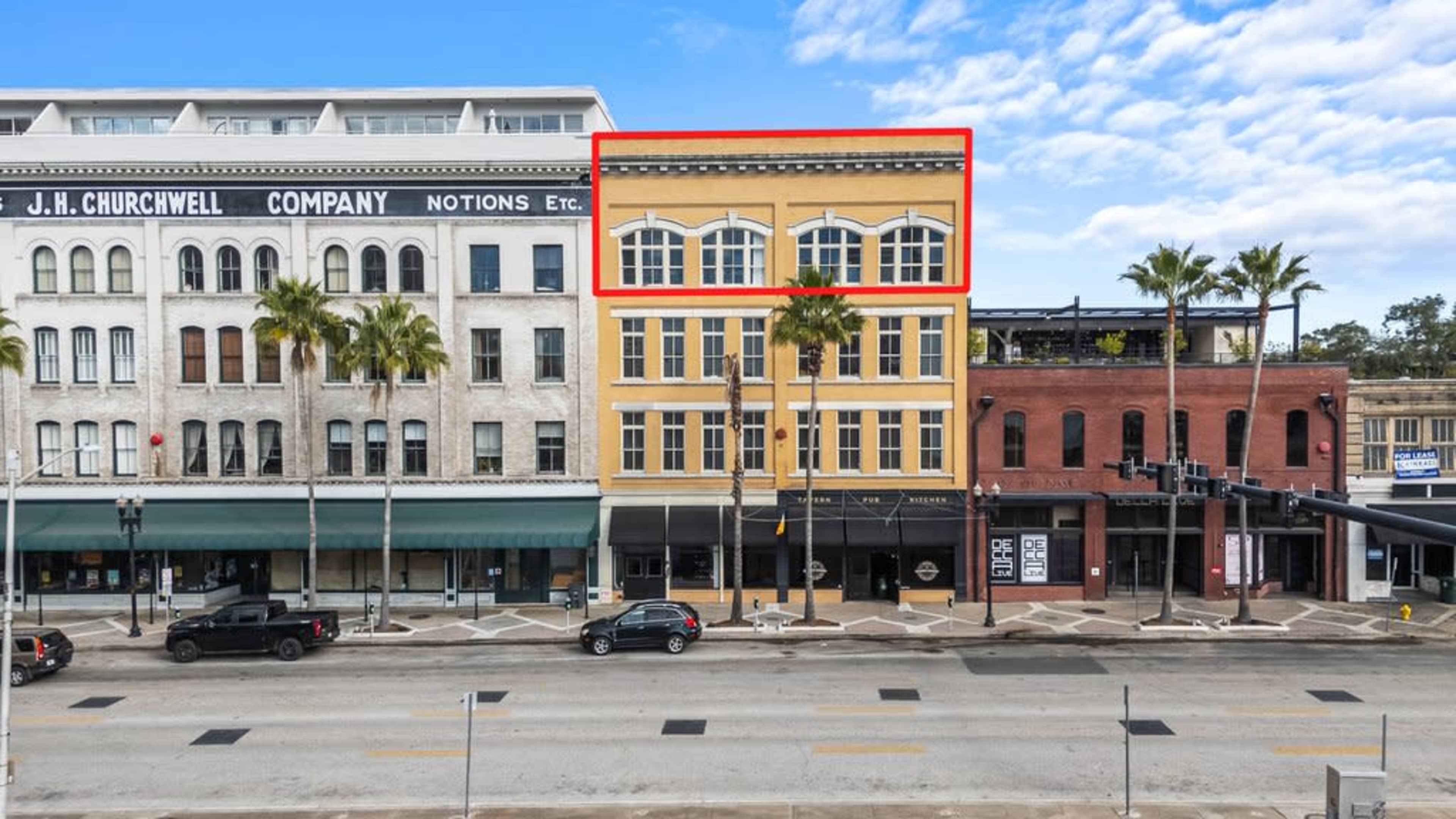 The image shows a row of commercial buildings along a street, with one building highlighted in red featuring large windows and a yellow facade.