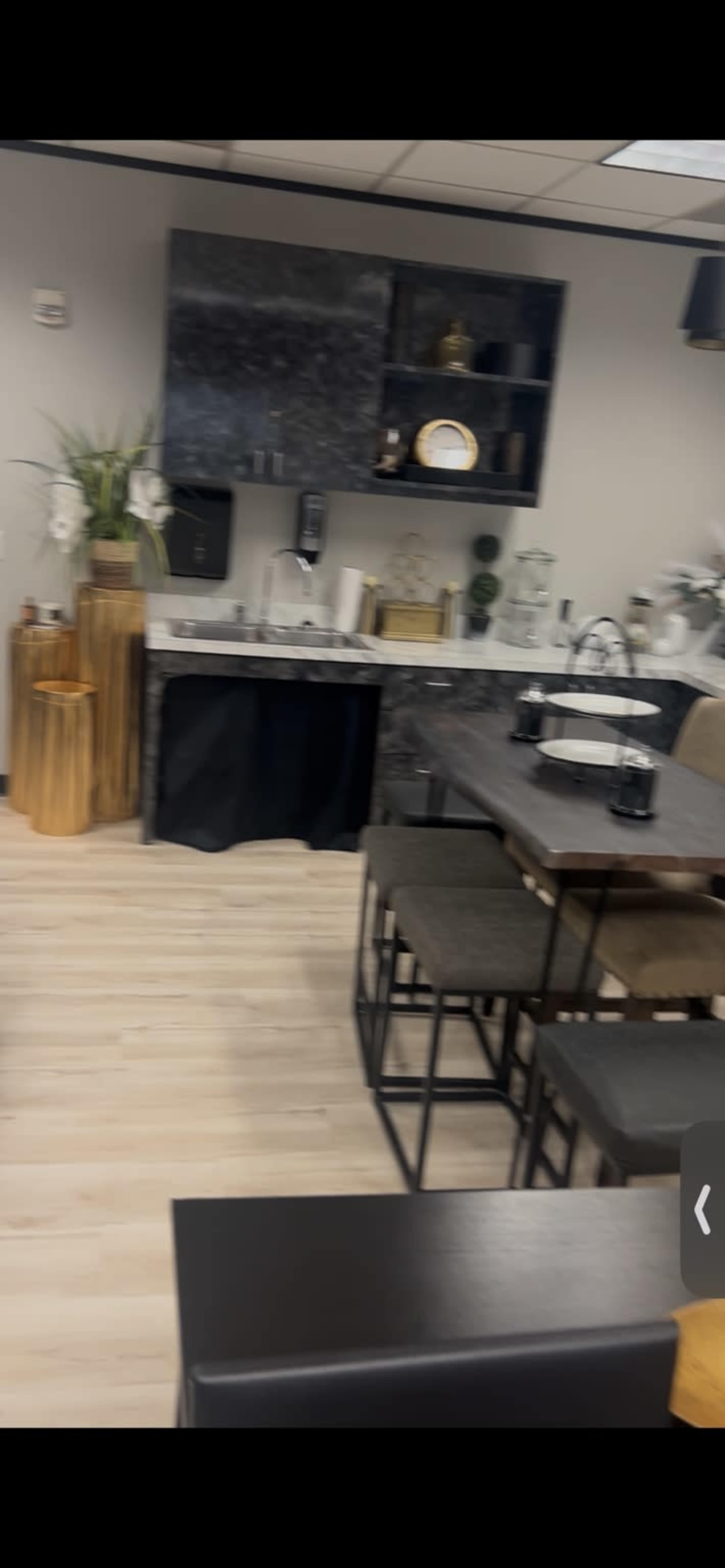 The image shows a modern kitchen area with a table and chairs, featuring minimalist decor and wooden accents.