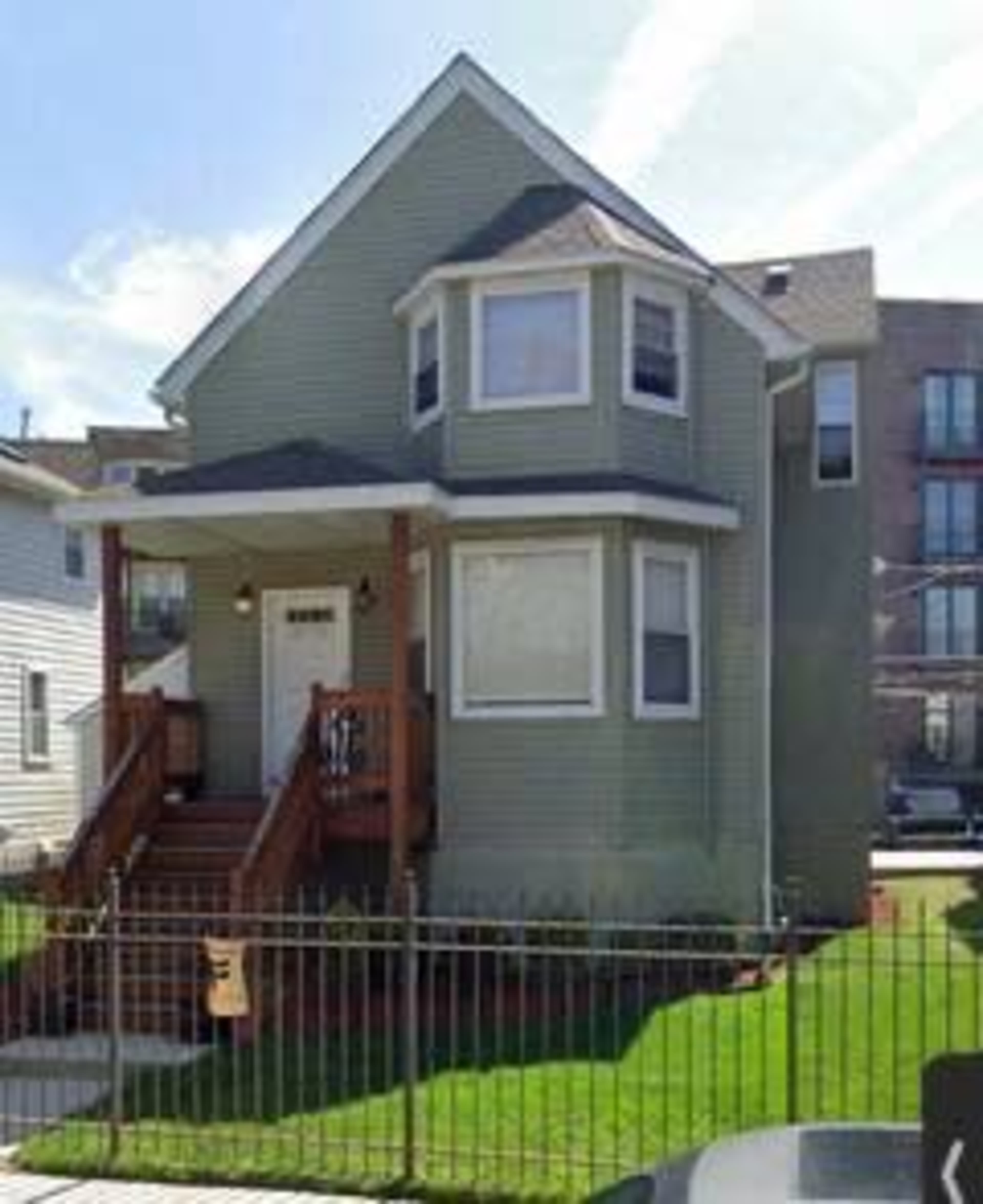 A two-story green house with a front porch and a fenced lawn.