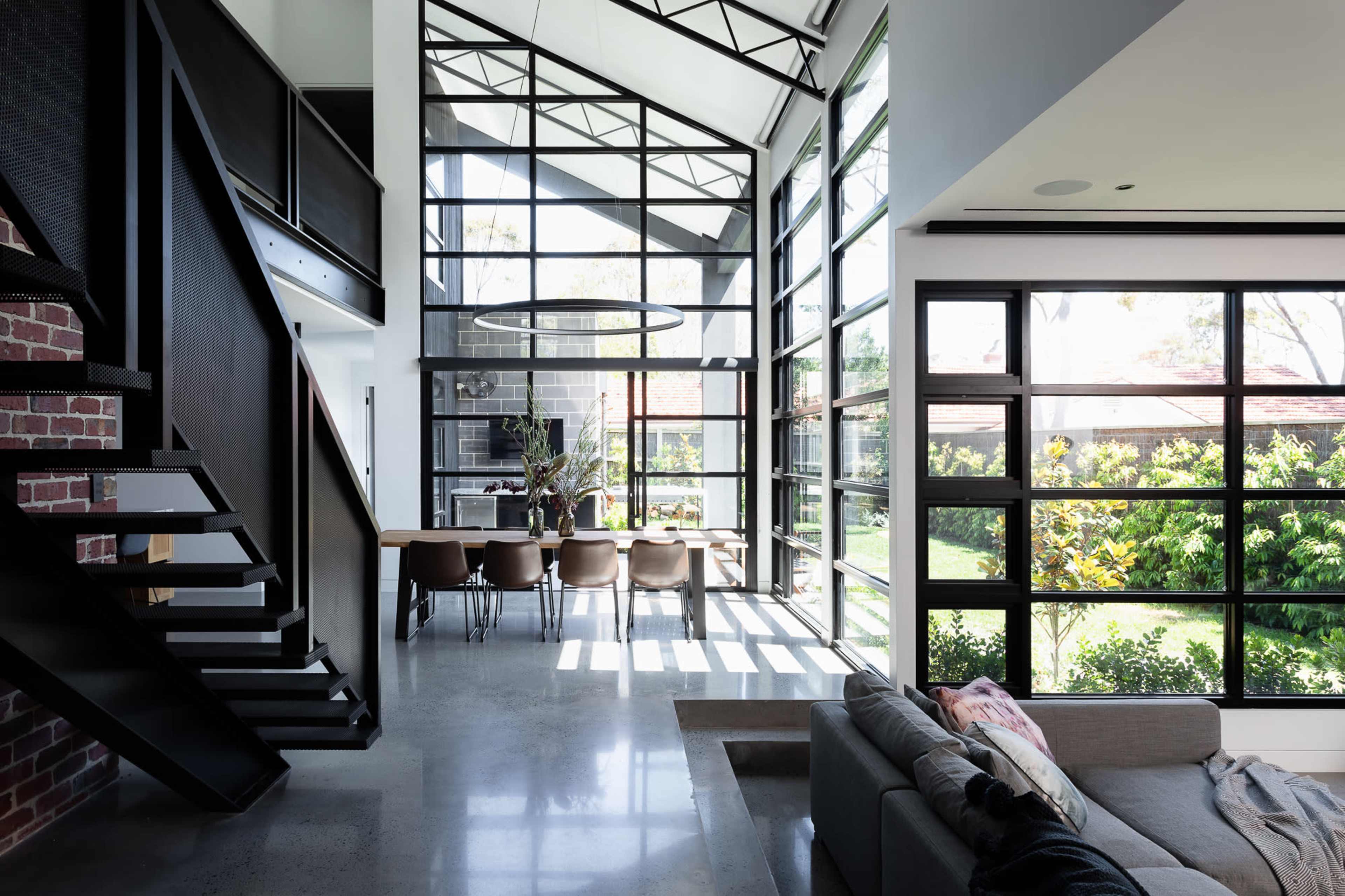 A modern, open-concept living space with large windows and a staircase leading to an upper level.