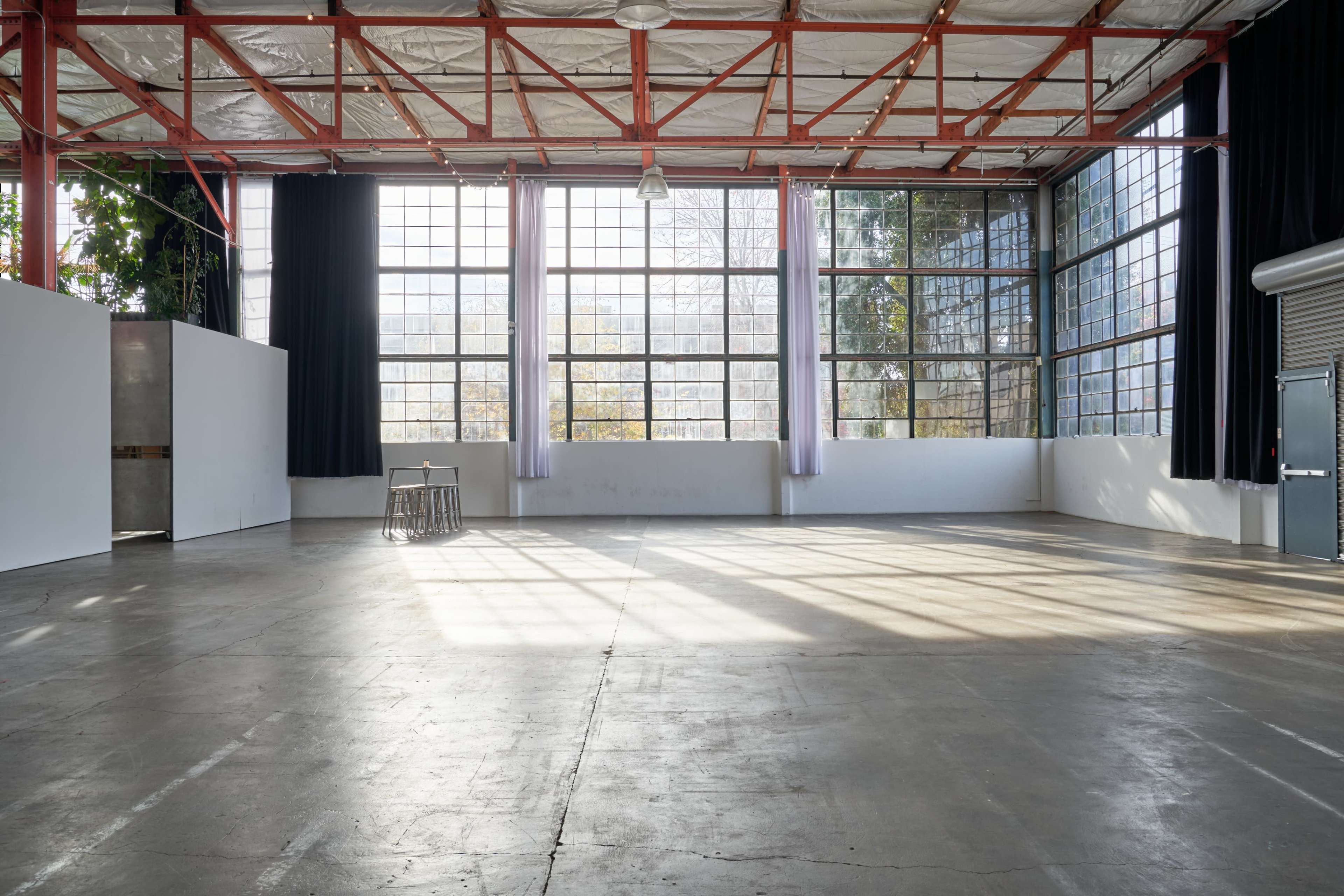 An empty industrial space with large windows, exposed red beams, and a concrete floor.