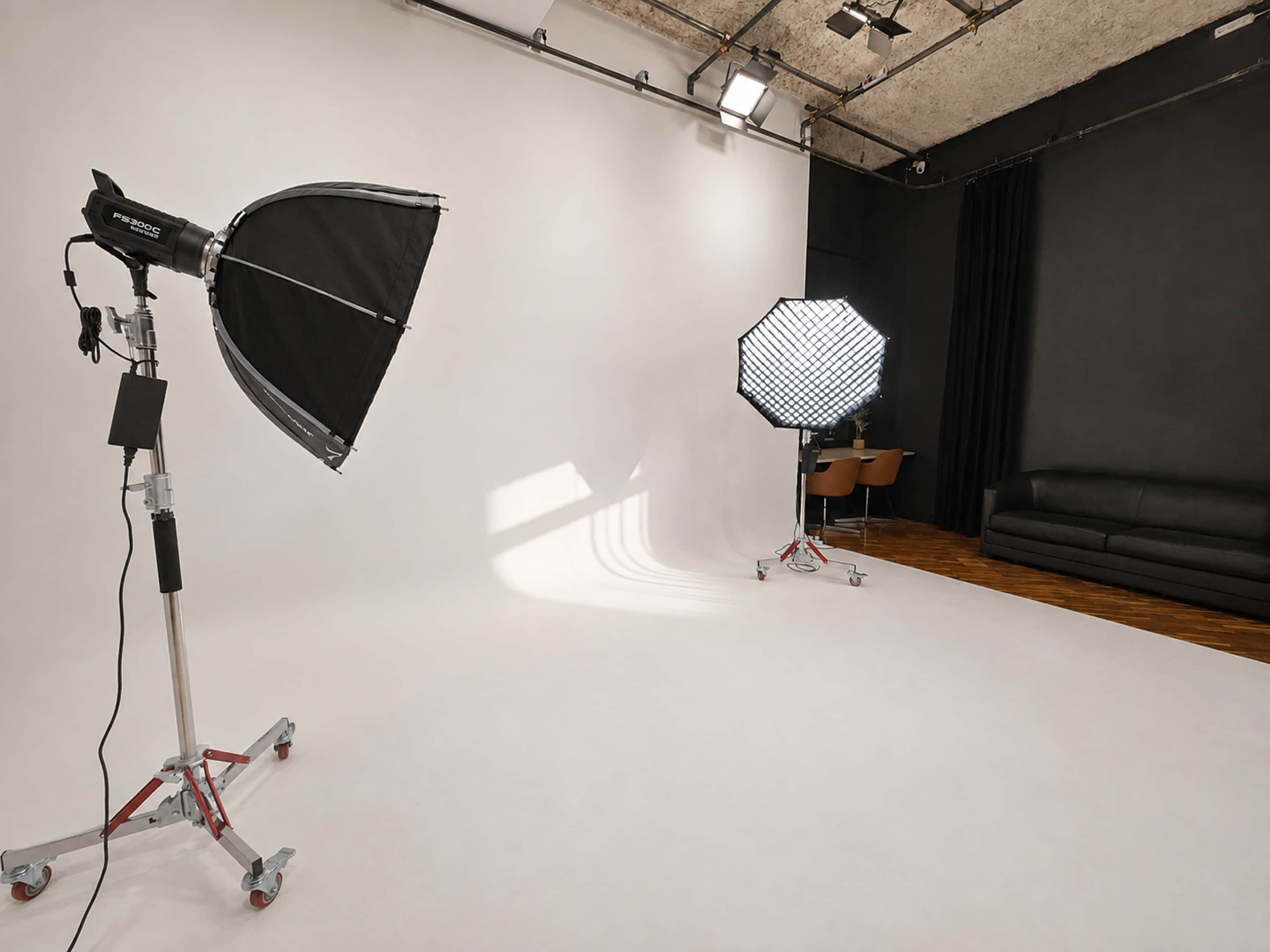 A photography studio features a white backdrop, two softbox lights, and a dark sofa in the corner.