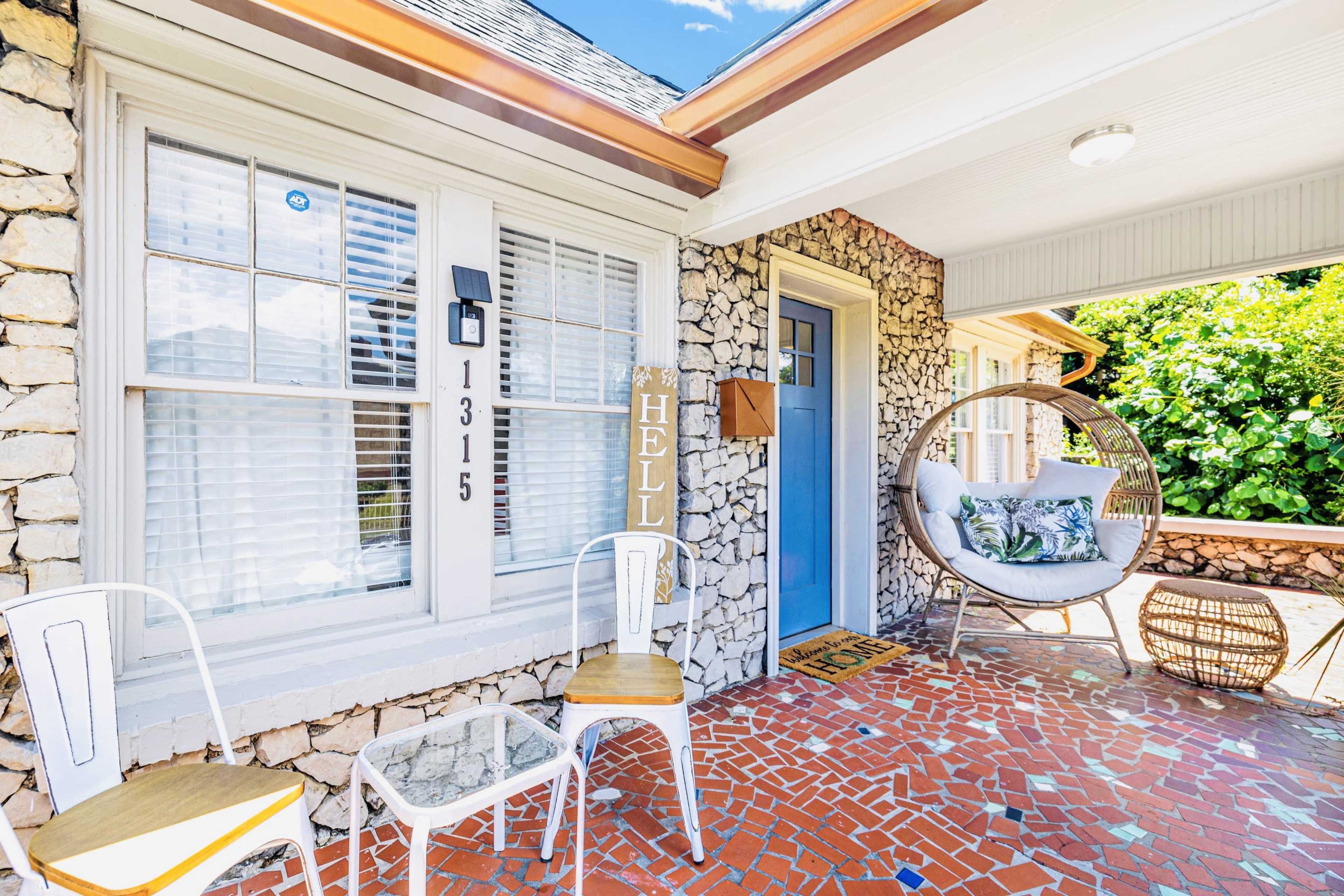 A front porch features a stone exterior, a blue door, a hanging chair, and mosaic tile flooring.