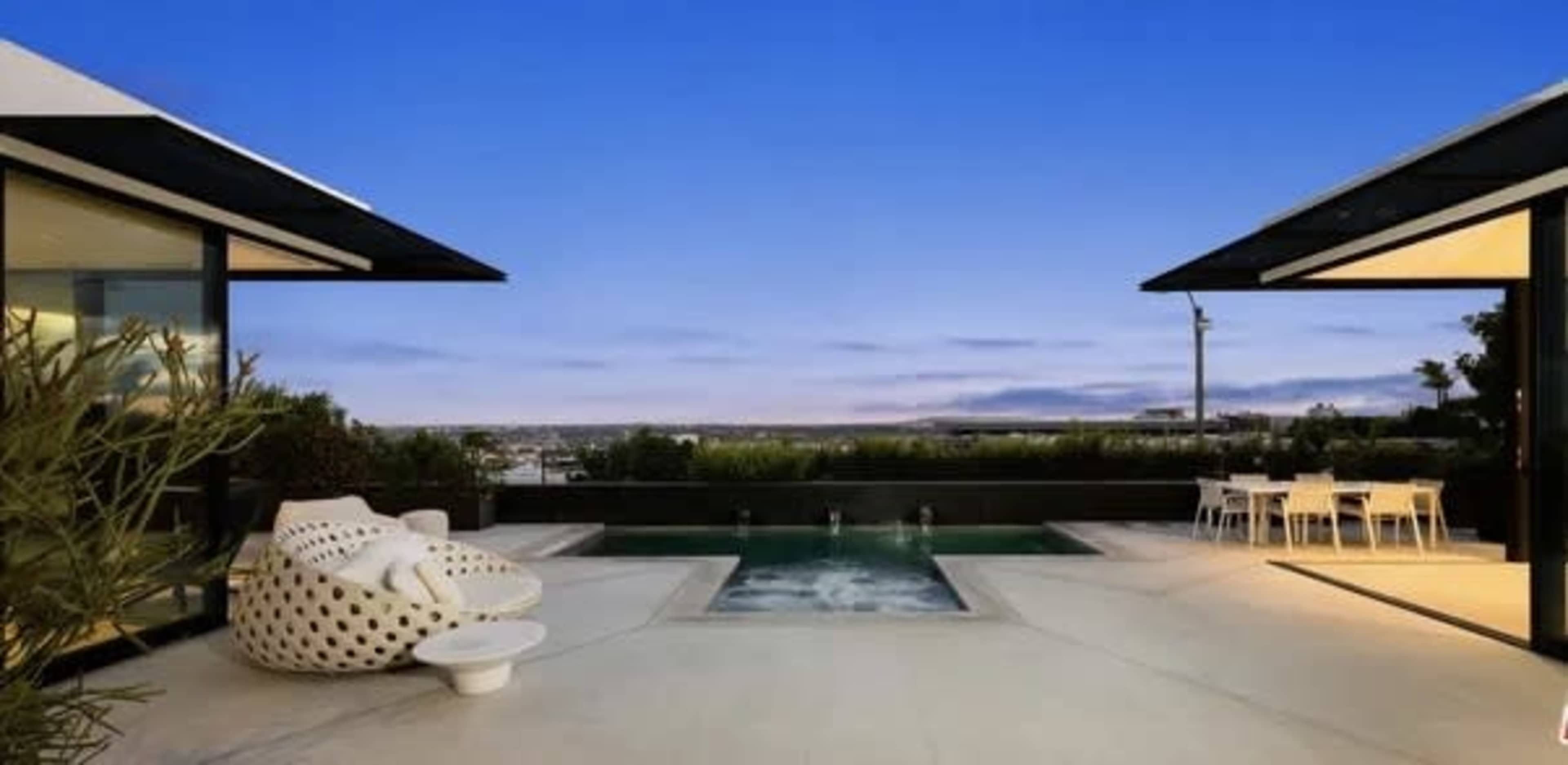 A modern outdoor space features a pool surrounded by sleek architecture and outdoor seating against a twilight sky.