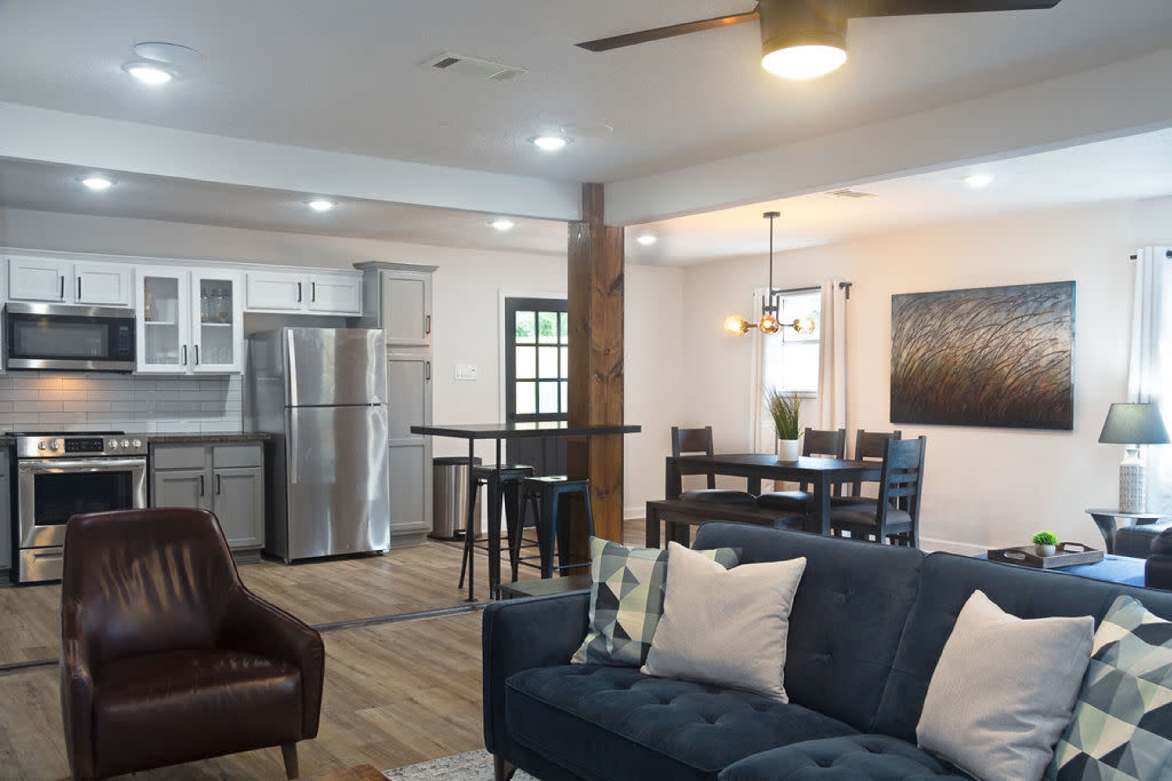 A modern open-concept living space with a kitchen, dining area, and seating area featuring a blue sofa and wooden accents.